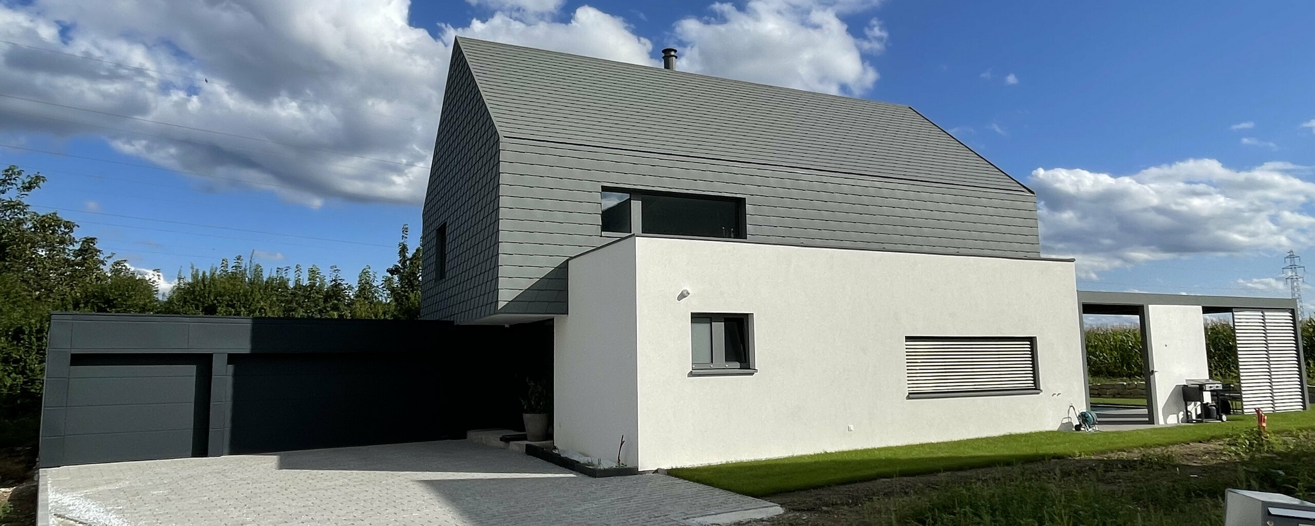 Vue éloignée de l'avant de cette maison moderne alsacienne. On aperçoit la cours pavée, le garage et les éléments en aluminium PREFA.