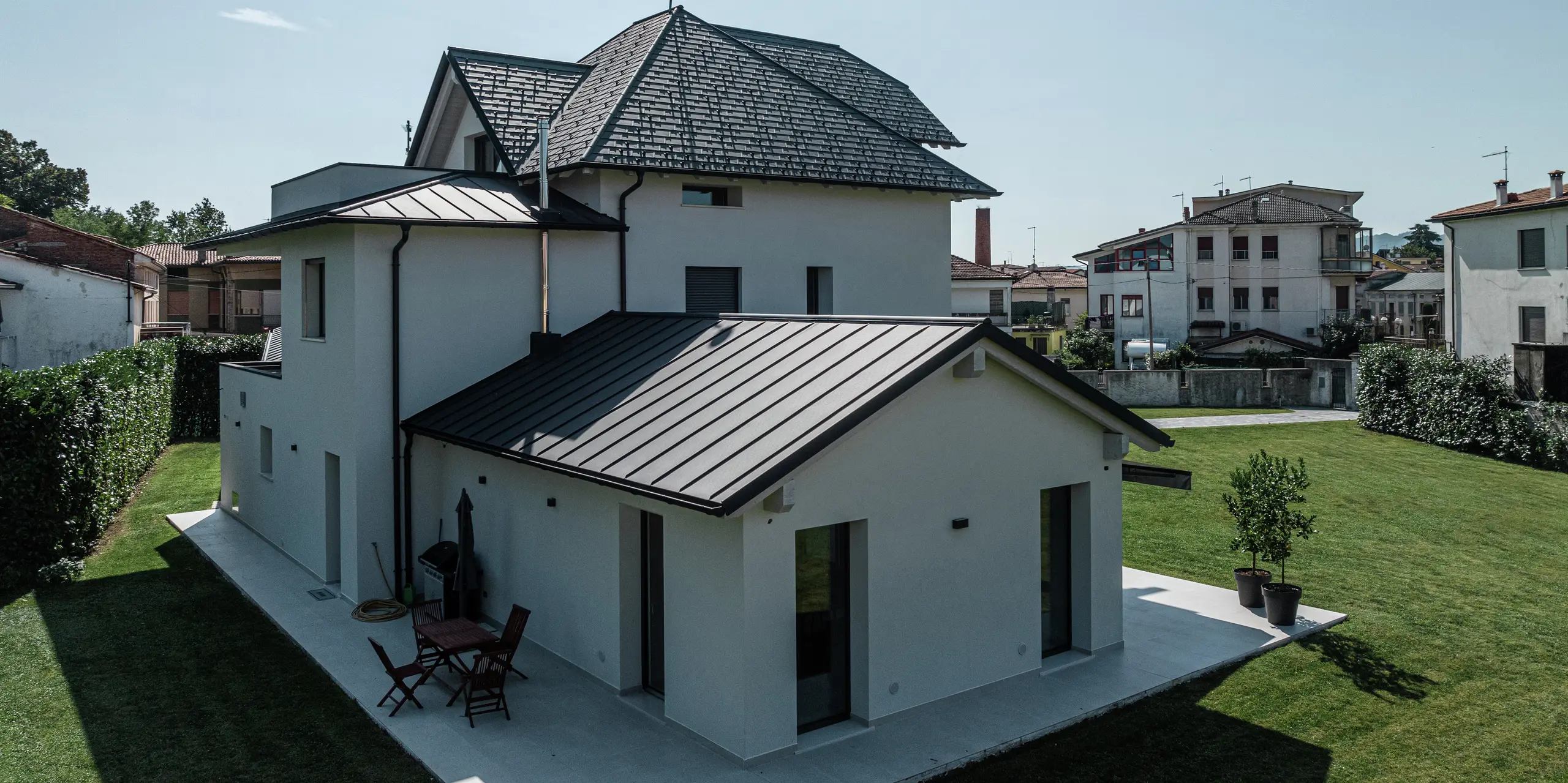 Vue arrière d'une maison familiale contemporaine à Marano Vicentino, en Italie, avec un toit en aluminium PREFA durable avec le revêtement P.10 de haute qualité en anthracite. Les dépendances adjacentes sont équipées d'une toiture robuste à double joint debout en aluminium. Le revêtement en aluminium de haute qualité allie esthétique et résistance aux intempéries.