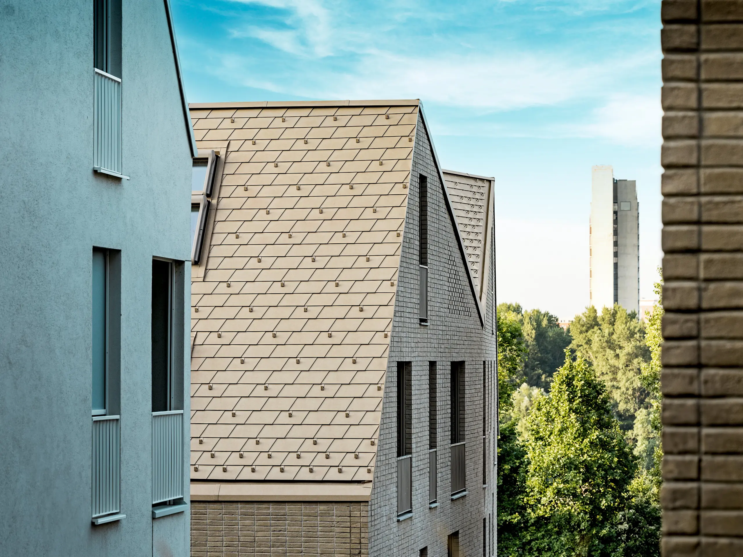 Gros plan sur la remarquable toiture du quartier Vydrica à Bratislava : des toits à forte pente, recouverts de tuiles en aluminium PREFA P.10 Brun Sable, posées avec précision, créent un motif rythmé qui attire immédiatement le regard. La finesse des lignes, la netteté des arêtes et la parfaite intégration entre la toiture et la façade soulignent la qualité architecturale. L’aluminium PREFA séduit par sa grande malléabilité, même pour les géométries complexes, sa résistance aux intempéries extrêmes et ses propriétés durables et nécessitant peu d’entretien – un matériau idéal pour les projets de construction urbaine exigeants aux fortes exigences esthétiques.