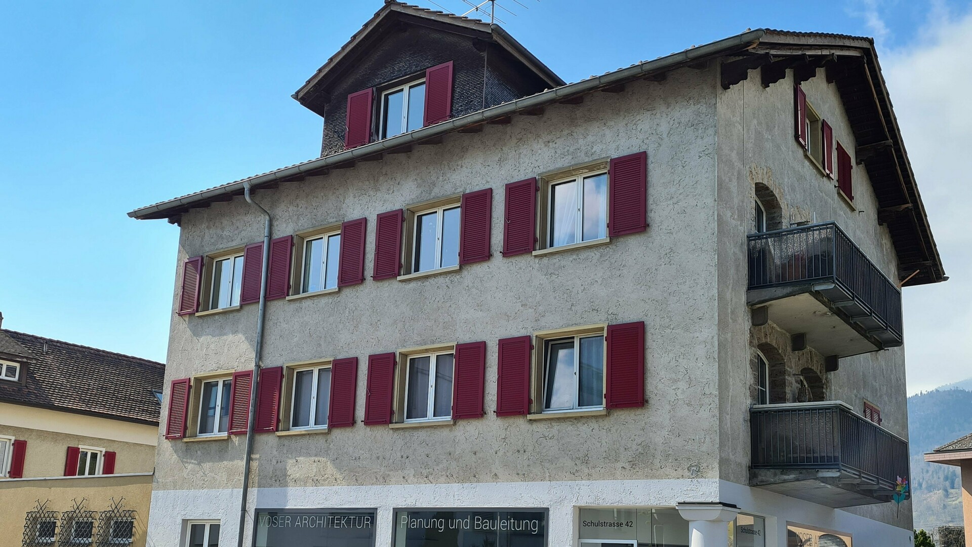 Vue depuis la rue d'un ancien bâtiment résidentiel et commercial avant la rénovation de la façade. La façade présente des signes visibles d'usure et une structure désuète. Au rez-de-chaussée se trouve le bureau d'architecture Voser avec de grandes vitrines. Dans le cadre de la rénovation, la façade sera modernisée à l'aide de panneaux composites en aluminium PREFABOND de couleur anthracite.