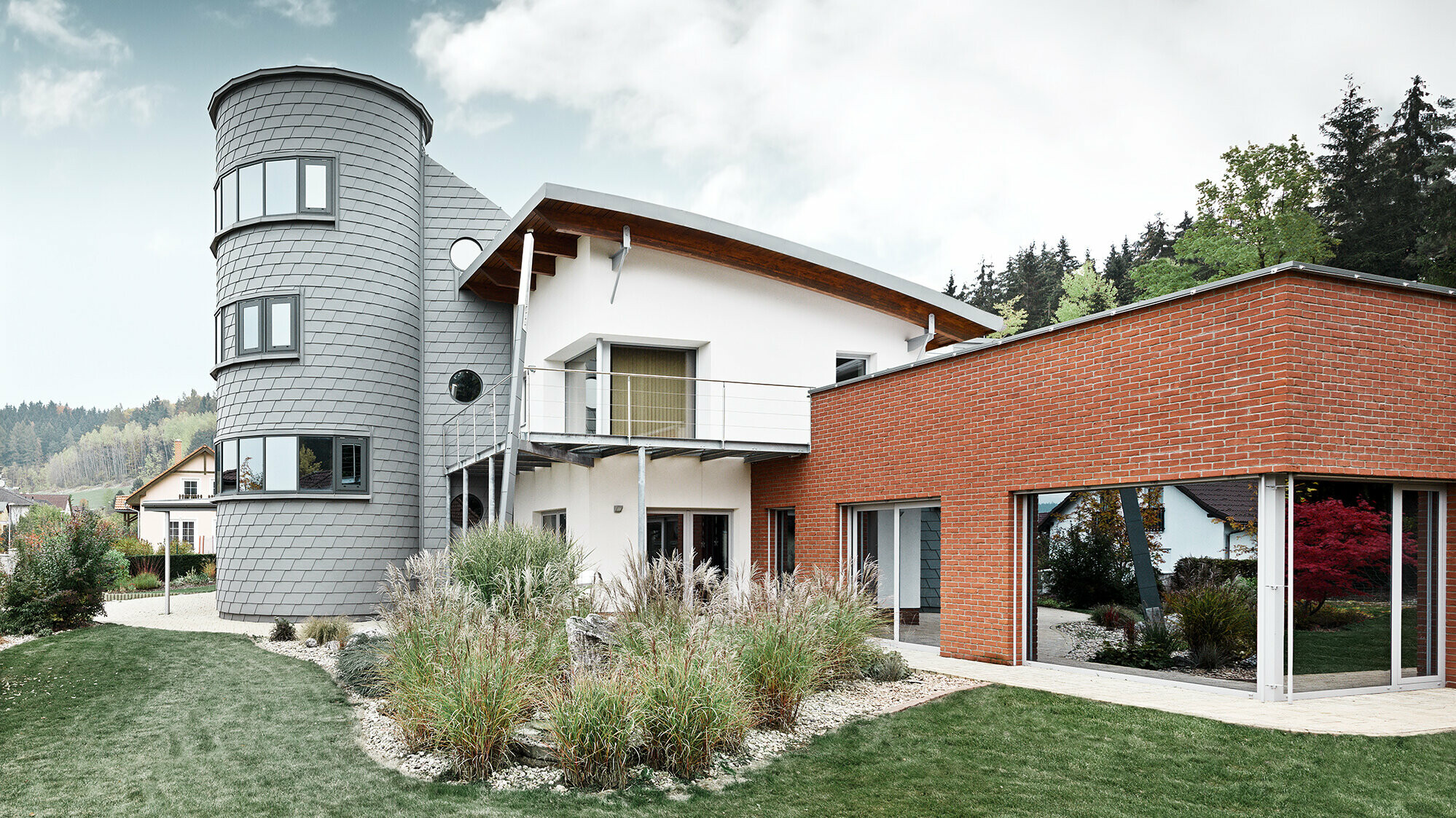 Maison individuelle avec extension de tour ; la tour ronde est revêtue du bardeau de façade PREFA couleur gris quartz 