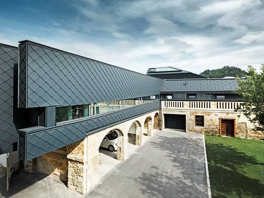 La cité administrative du district de Völkermarkt combine anciens et nouveaux bâtiments : le rez-de-chaussée a conservé ses vieux murs en pierre, tandis que l’étage supérieur est revêtu du losange de toiture moderne de PREFA 29 × 29 couleur anthracite.