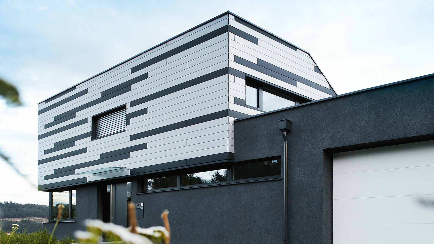 Maison individuelle moderne présentant une conception de façade créative. Les Sidings PREFA couleur argent et anthracite mat ont été posés mélangés.