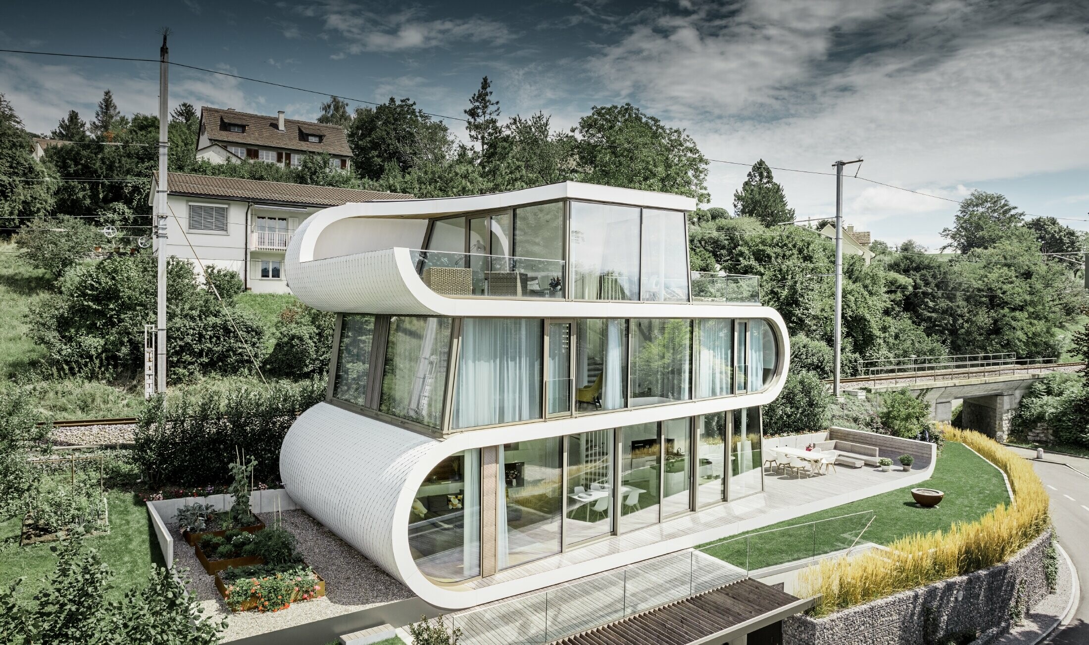 Maison individuelle très moderne conçue par l’architecte Stefan Camenzind de Zurich ; une bande ondulée relie les différents étages entre eux. Les courbures ont été habillées avec le losange de toiture PREFA, en petit format, couleur blanc pur. La maison présentant de nombreuses et vastes surfaces vitrées, elle donne une grande impression d’ouverture.