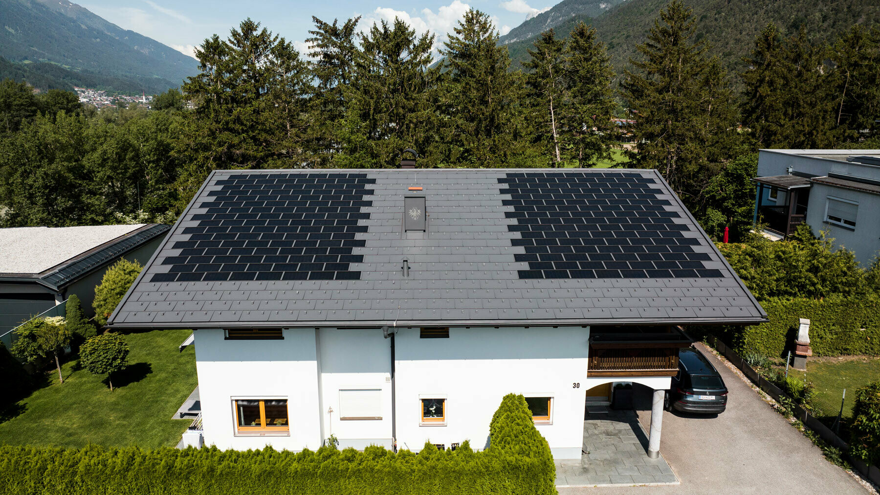 La photo montre une maison individuelle recouverte avec la tuile solaire PREFA petit format et le R.16 couleur P.10 gris sombre dans un environnement rural.