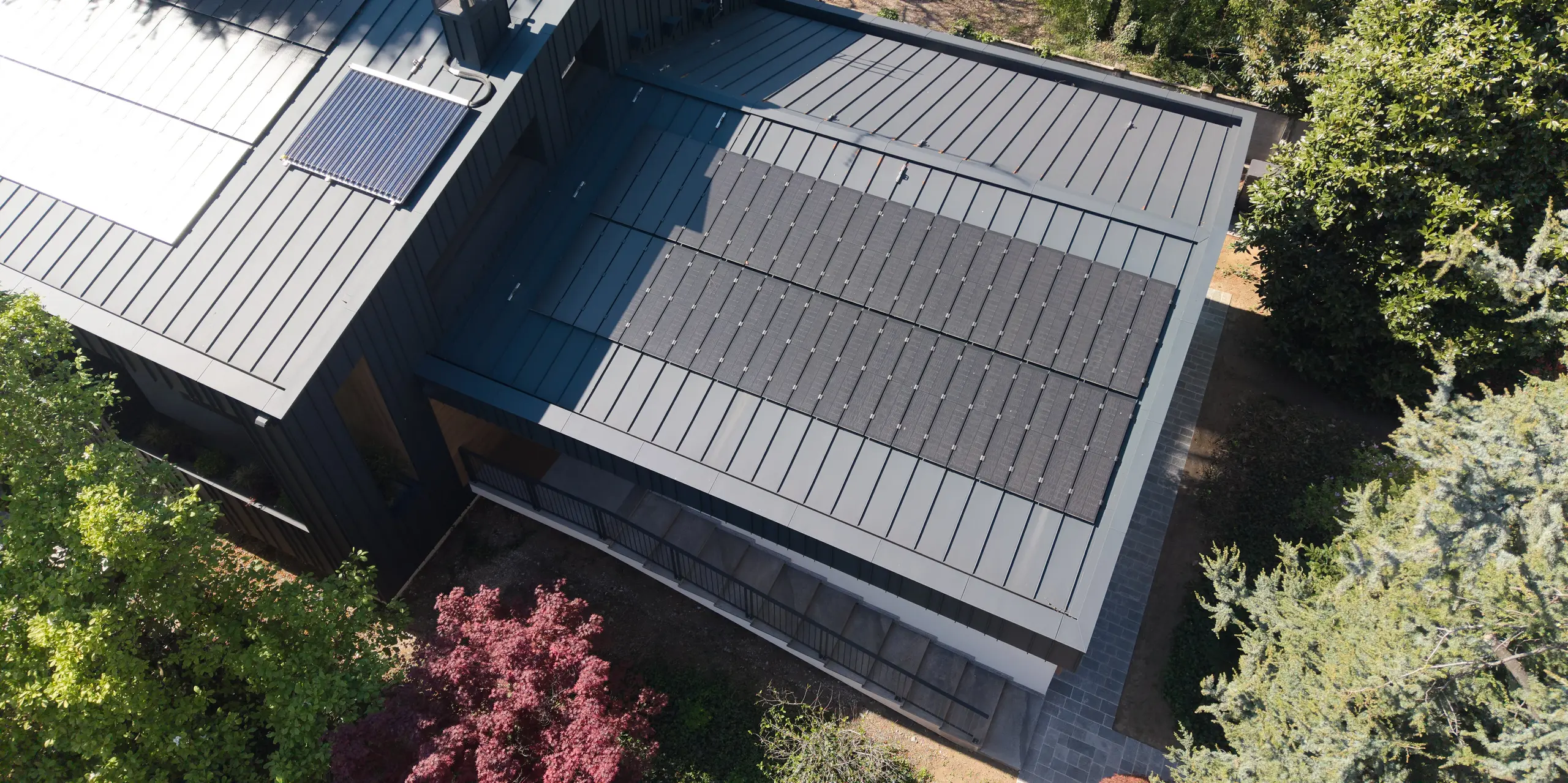 Vue aérienne de la Villa Castellanza, dotée d'une toiture PREFALZ couleur P.10 Anthracite et de modules solaires PREFALZ innovants. La toiture en aluminium, au design précis, impressionne par ses lignes épurées et son élégance. Production d'énergie durable, haute résistance aux intempéries et qualité irréprochable des matériaux PREFALZ allient architecture, fonctionnalité et design avec brio.