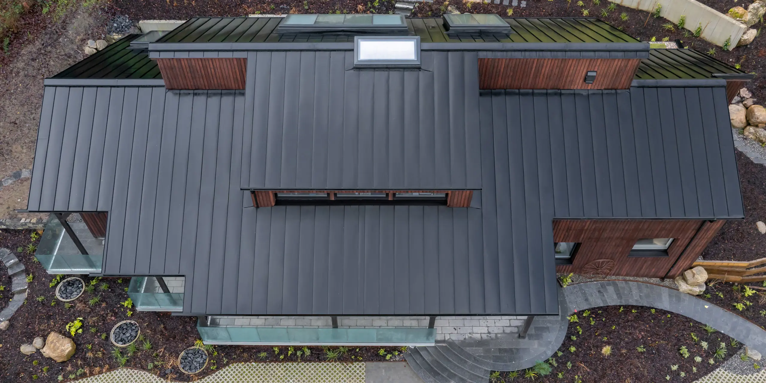 Vue aérienne de la Maison Holywell à Sligo : les surfaces de toiture clairement structurées de la toiture en aluminium PREFALZ P.10 Noir révèlent tout leur potentiel vu du ciel. Les joints debout parallèles structurent avec précision la toiture et guident le regard à travers les lucarnes et les différents niveaux. L’uniformité de la surface souligne la qualité de la réalisation. L’aluminium PREFA impressionne par sa durabilité, sa résistance à la corrosion et son fonctionnement optimal même dans des conditions climatiques difficiles.