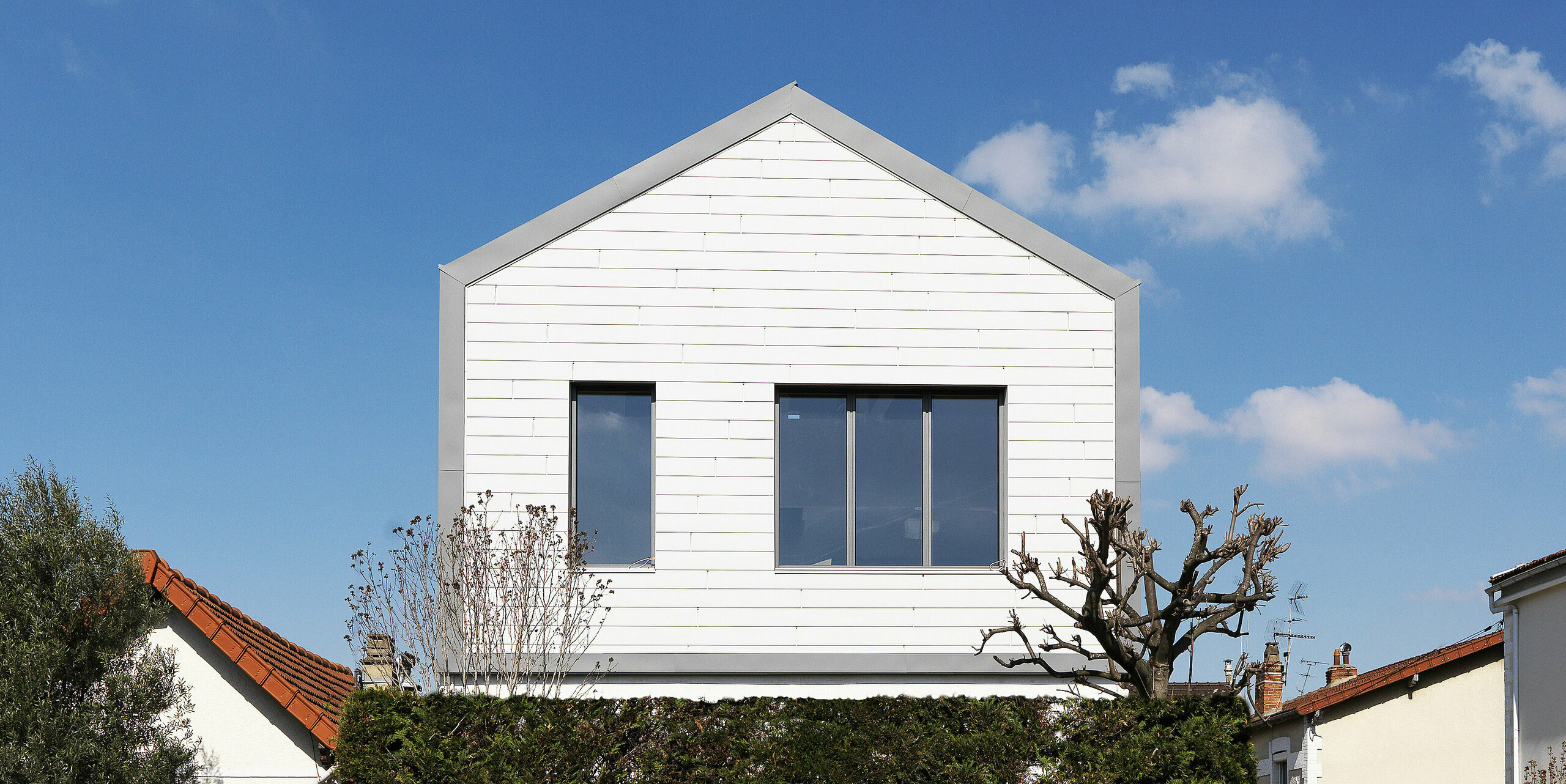 Vue sur la rue d'une maison familiale à Houilles (France). Pour le bâtiment, les Siding PREFA en P.10 blanc pur ont été combinés en façade et PREFALZ en P.10 gris souris en toiture et façade.