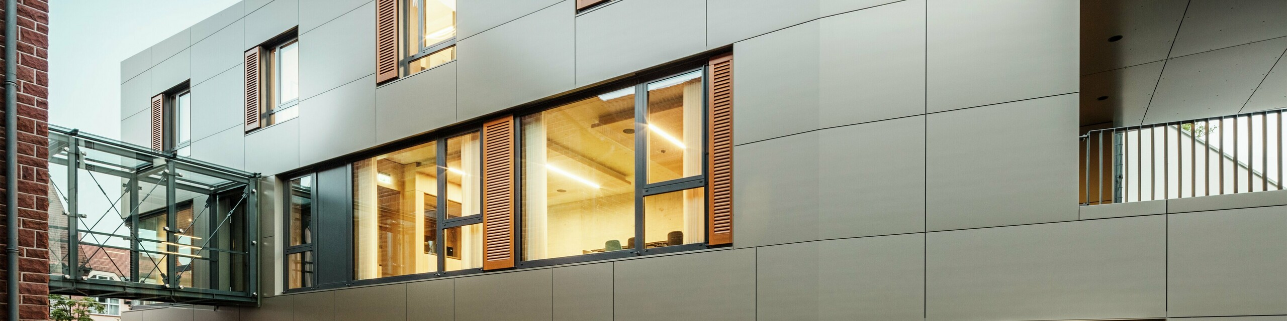 Façade moderne de la mairie d'Alzenau en Allemagne avec des panneaux composites en aluminium PREFA en bronze, combinés à des volets et des surfaces végétalisées. Le revêtement en aluminium haut de gamme garantit un aspect élégant et durable et est idéal pour les projets de construction durables. Ici, le site est bien visible.