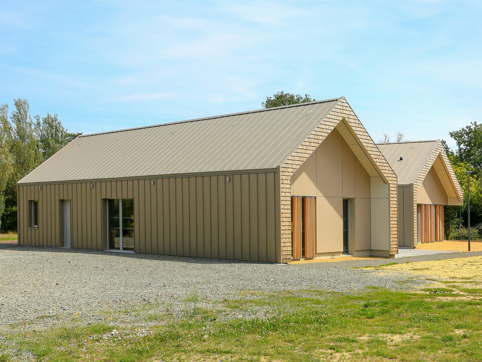 Maison de jeunesse moderne à Mûrs-Erigné, France, avec toiture PREFALZ durable et revêtement de façade en bronze. La toiture en aluminium à joint debout de PREFA impressionne par sa grande résistance aux intempéries et son aspect élégant - idéale pour les projets de construction durables et nécessitant peu d'entretien. La palette de couleurs élégante montre une intégration parfaite dans l'environnement.