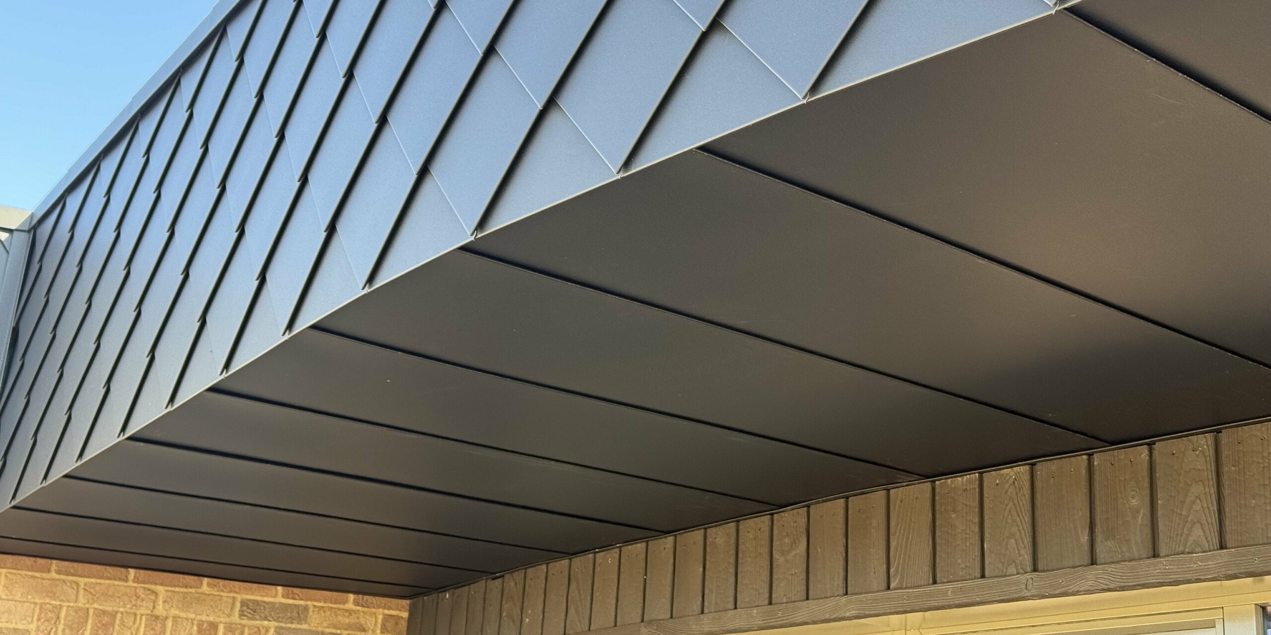 Vue détaillée de la façade moderne d'une maison écologique du projet « Doone Brae Farm ». Dans la partie supérieure, les losanges de façade PREFA petit format, couleur P.10 Anthracite, créent des accents saisissants. Robustes et résistants aux intempéries, ces losanges en aluminium sont durables et faciles d'entretien, des atouts indéniables pour une architecture durable. La face inférieure est complétée par des panneaux d'aluminium lisses. Dans la partie inférieure de la façade, les surfaces en briques de parement aux tons chauds offrent un contraste de matériaux harmonieux. L'alliance de l'aluminium et des briques de parement confère à ce bâtiment une esthétique intemporelle et une fonctionnalité optimale, le rendant véritablement remarquable.