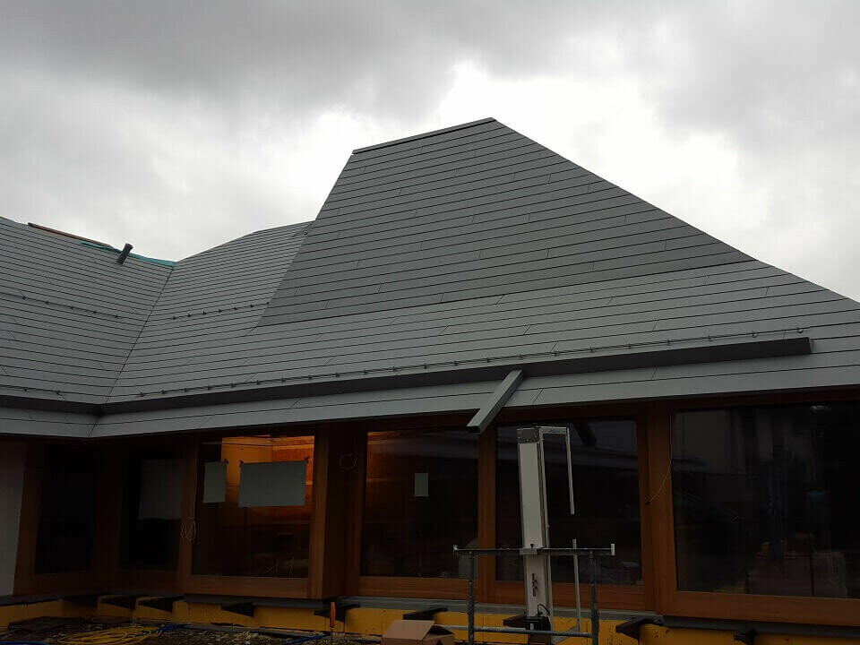 Neubau Kindergarten Riehen mit einem tief vorgezogenen Dach aus grossformatigen Schindeln aus Prefalz