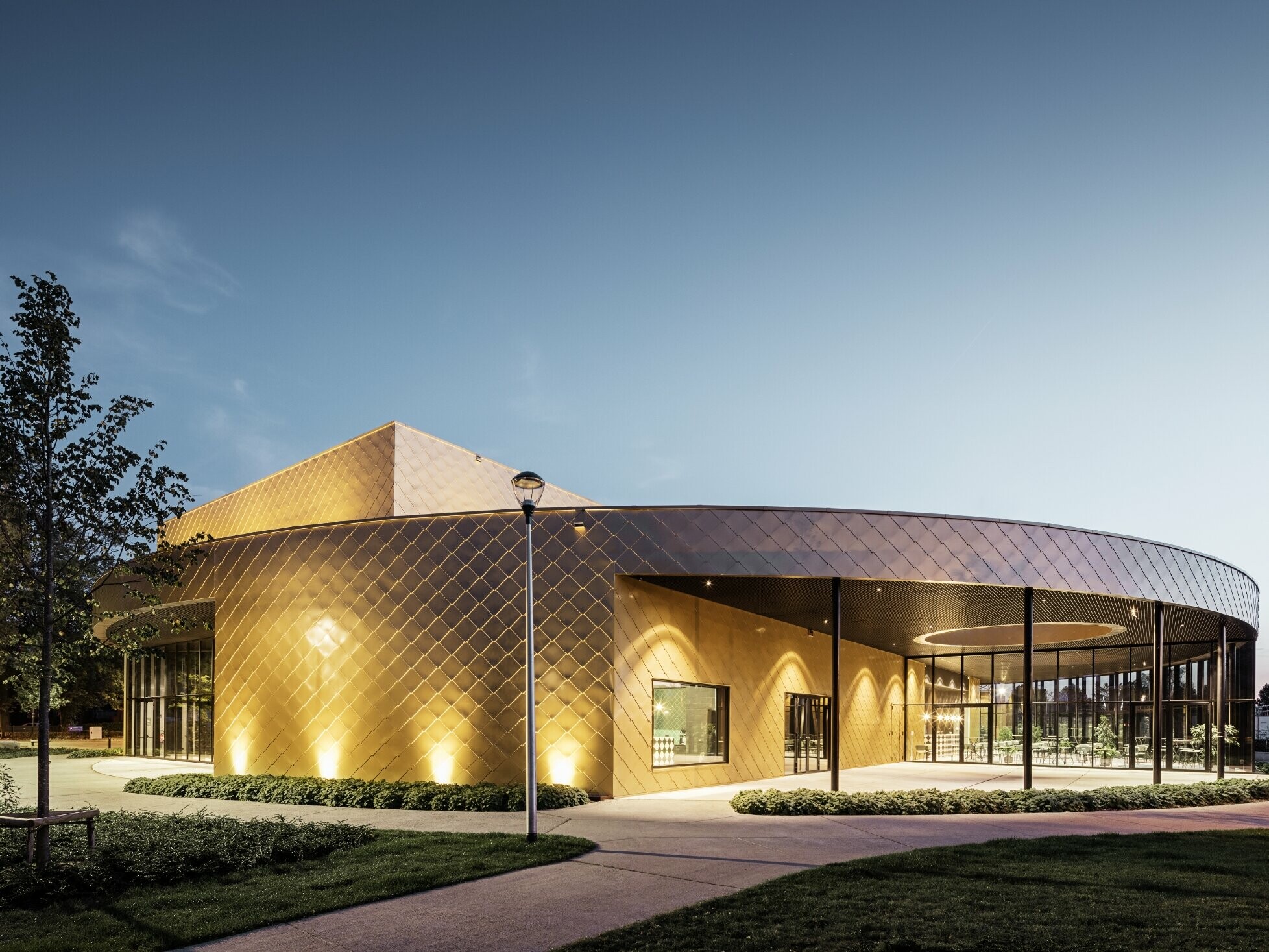 Photo du centre culturel de Kapellen au crépuscule avec losange de façade PREFA en 44 × 44 couleur mayagold