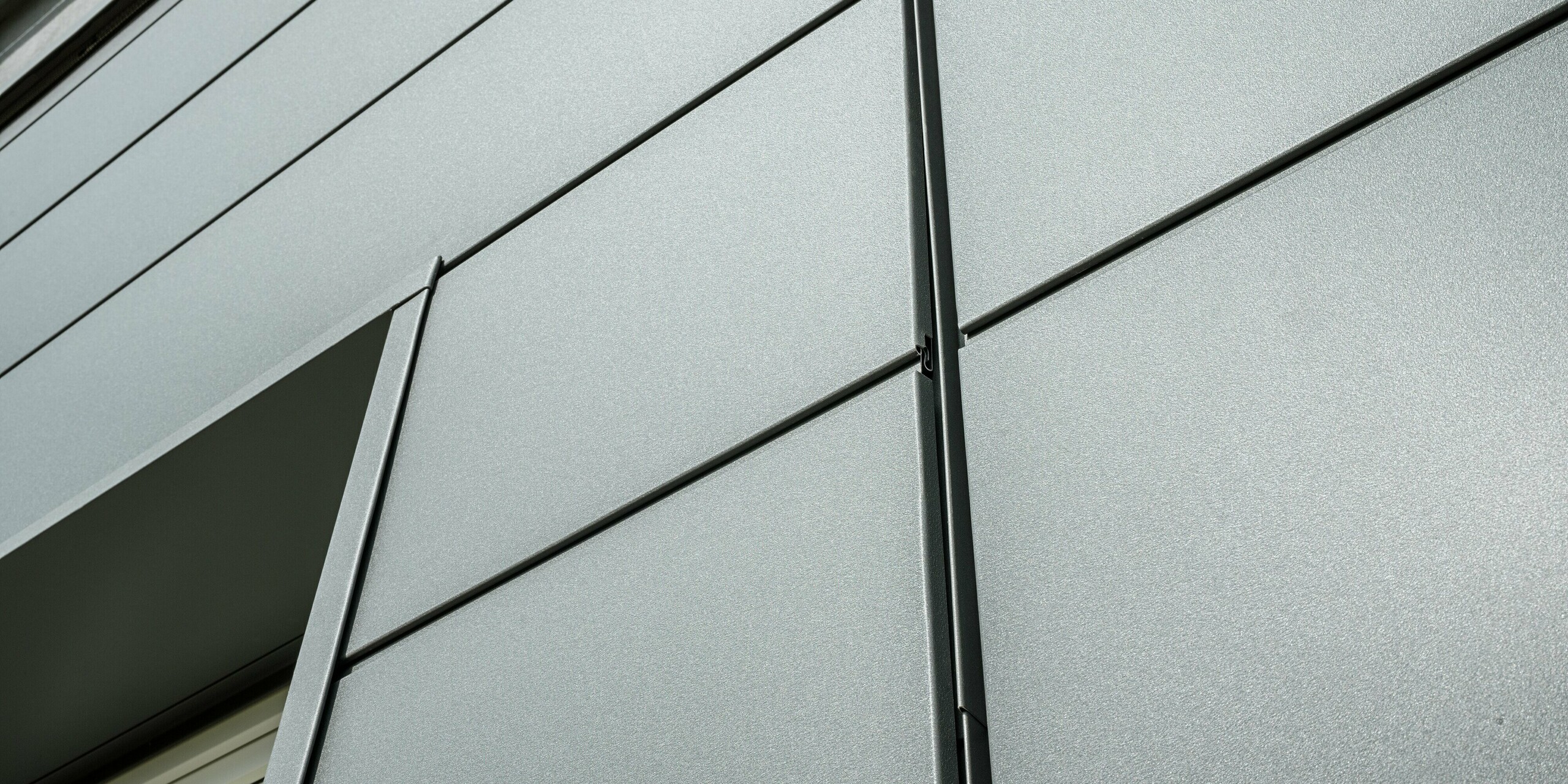 La façade du bâtiment de la guilde des ramoneurs à Bindlach est revêtue d'un bardage moderne PREFA P.10 gris sombre. Les panneaux d'aluminium à la structure apparente sont non seulement esthétiques, mais aussi extrêmement résistants aux intempéries. Le gros plan révèle clairement la précision de la pose des panneaux métalliques et l'élégance minimaliste des lignes.