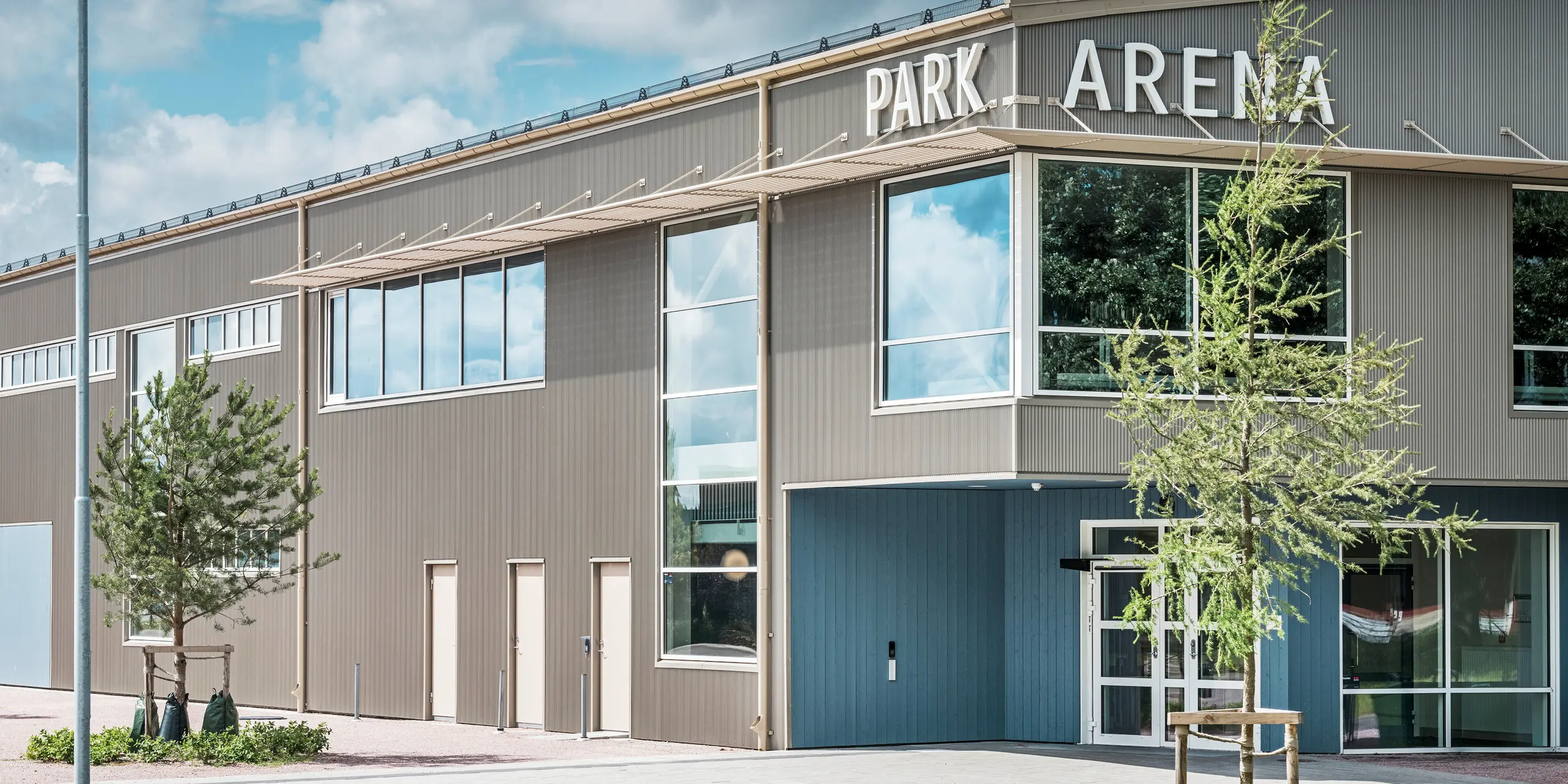 Zone d'entrée du Park Arena de Värnamo, en Suède, avec un design de façade moderne sous la forme du profil extrudé triangle PREFA en bronze. La façade en aluminium durable et résistante aux intempéries confère à la salle de sport de 3 300 m² un aspect élégant et saisissant. Le profil dentelé PREFA crée des effets d'ombre et de lumière fascinants qui mettent en valeur la conception architecturale de l'arène.