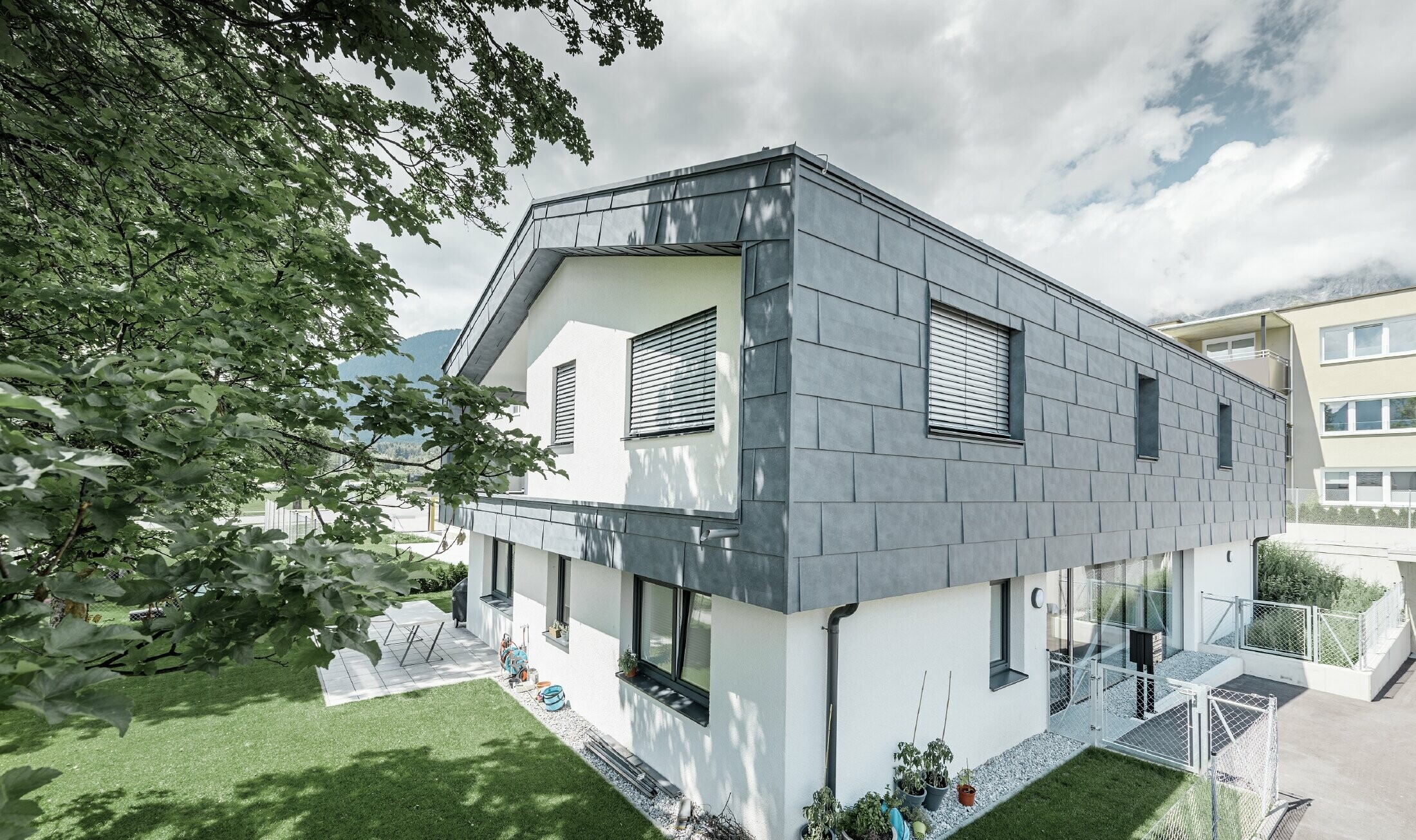 Structure moderne d’un bâtiment d’habitation avec toit à deux pans et sans avancée de toit ; l’habillage de façade a été réalisé avec le panneau de façade FX.12 PREFA couleur gris pierre.