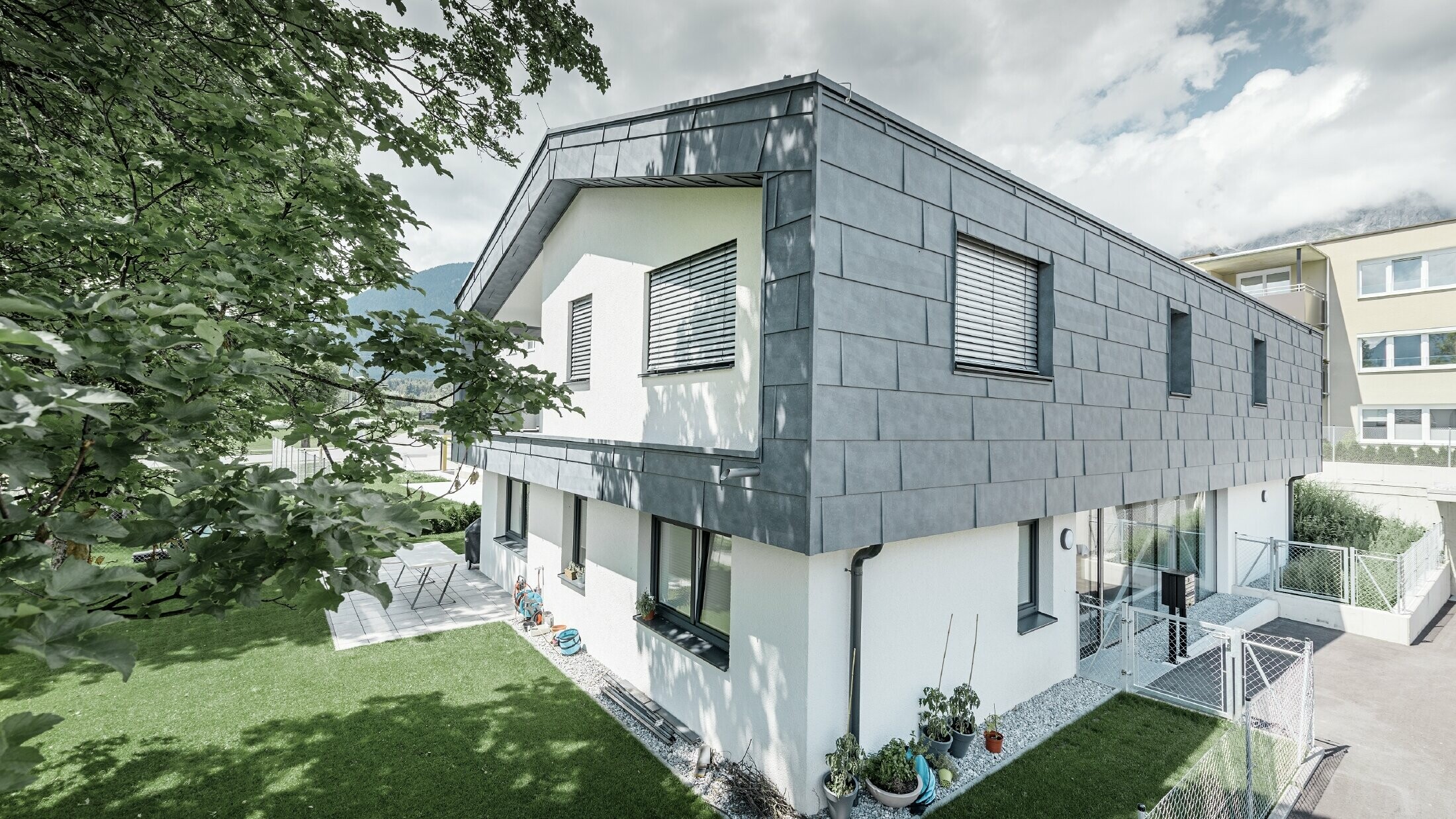 Structure moderne d’un bâtiment d’habitation avec toit à deux pans et sans avancée de toit ; l’habillage de façade a été réalisé avec le panneau de façade FX.12 PREFA couleur gris pierre.