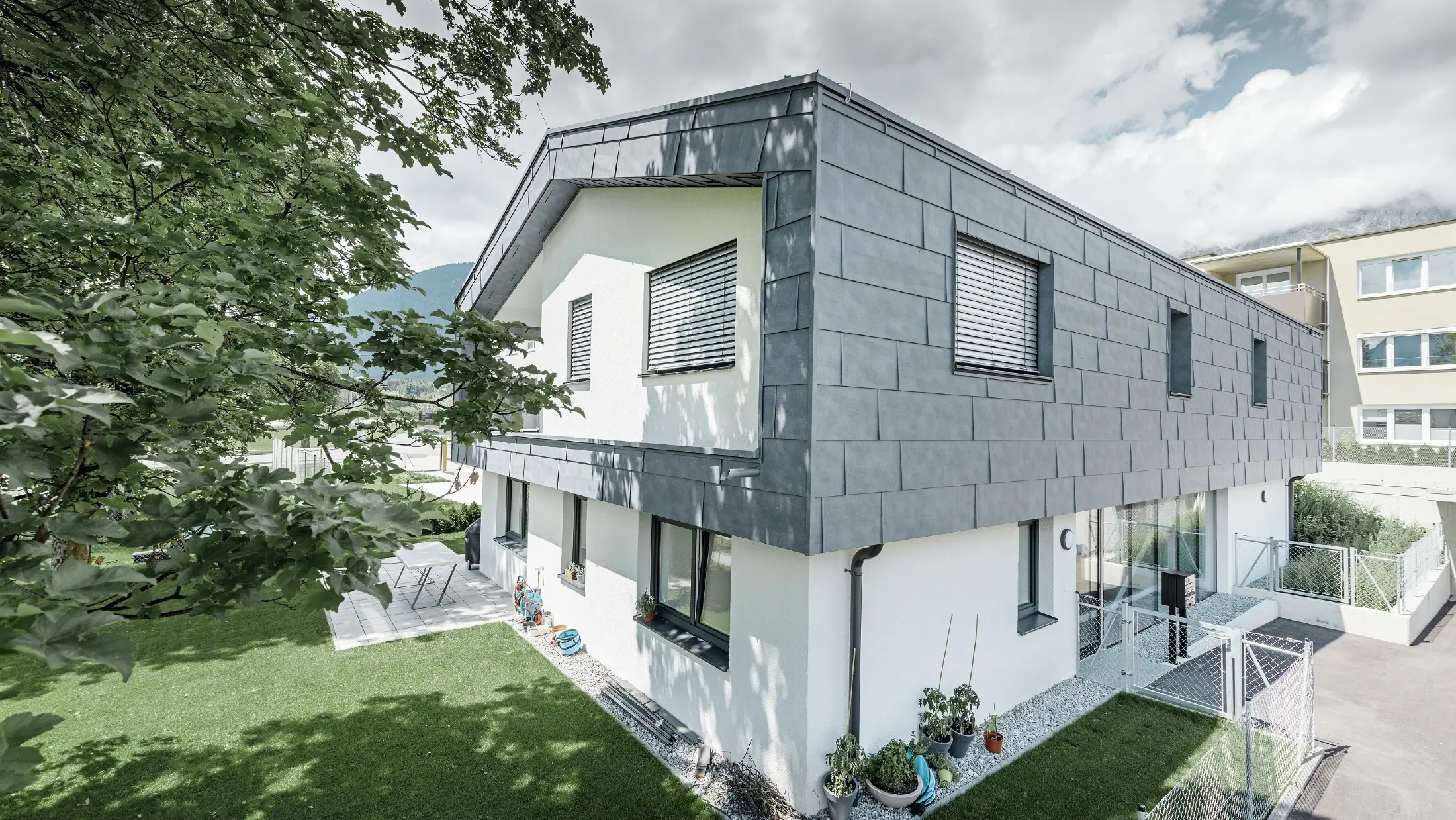 Structure moderne d’un bâtiment d’habitation avec toit à deux pans et sans avancée de toit ; l’habillage de façade a été réalisé avec le panneau de façade FX.12 PREFA couleur gris pierre.