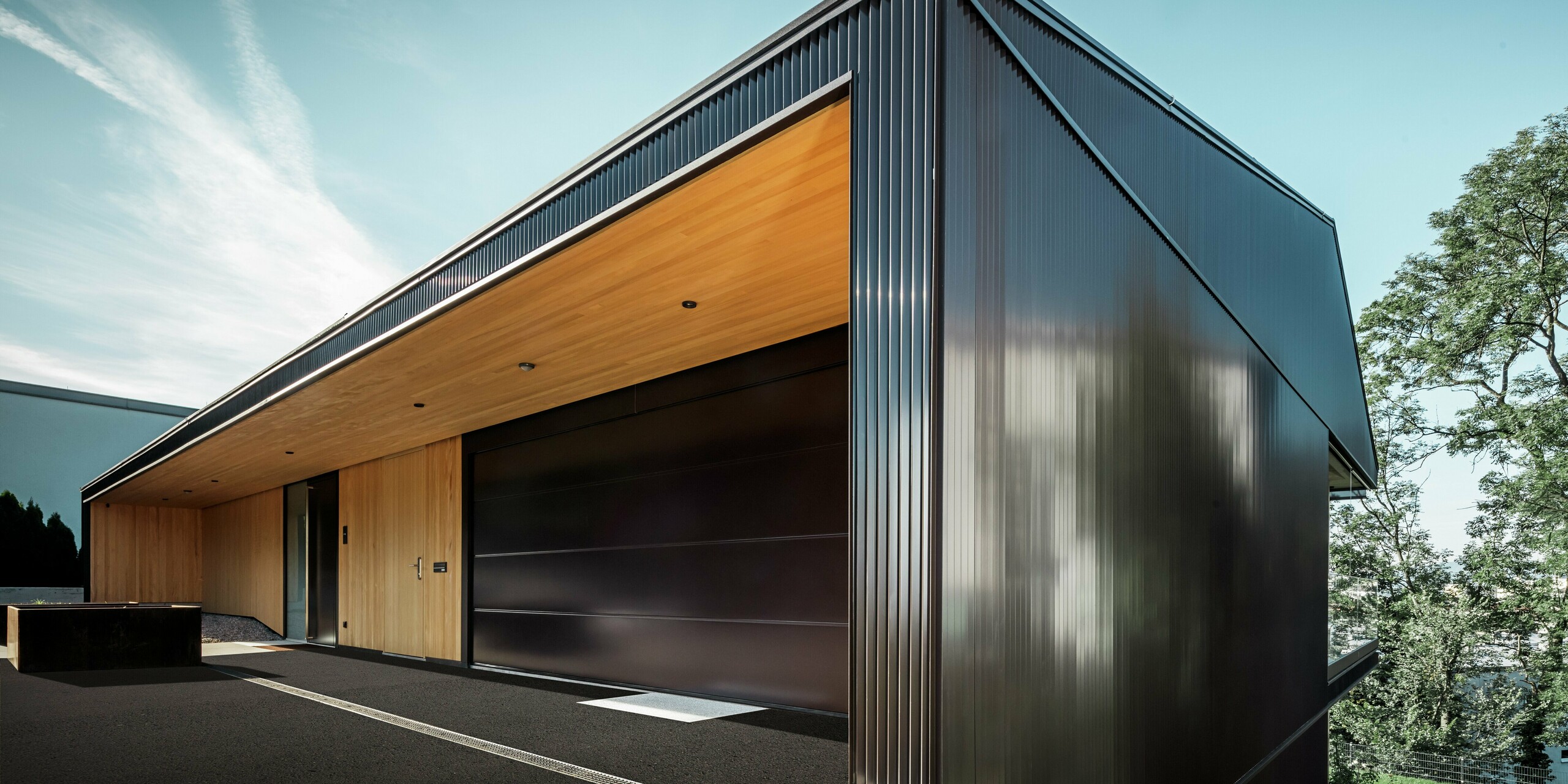 Entrée de garage d’une maison individuelle, la façade est recouverte de profils triangle PREFA couleur brun foncé.
