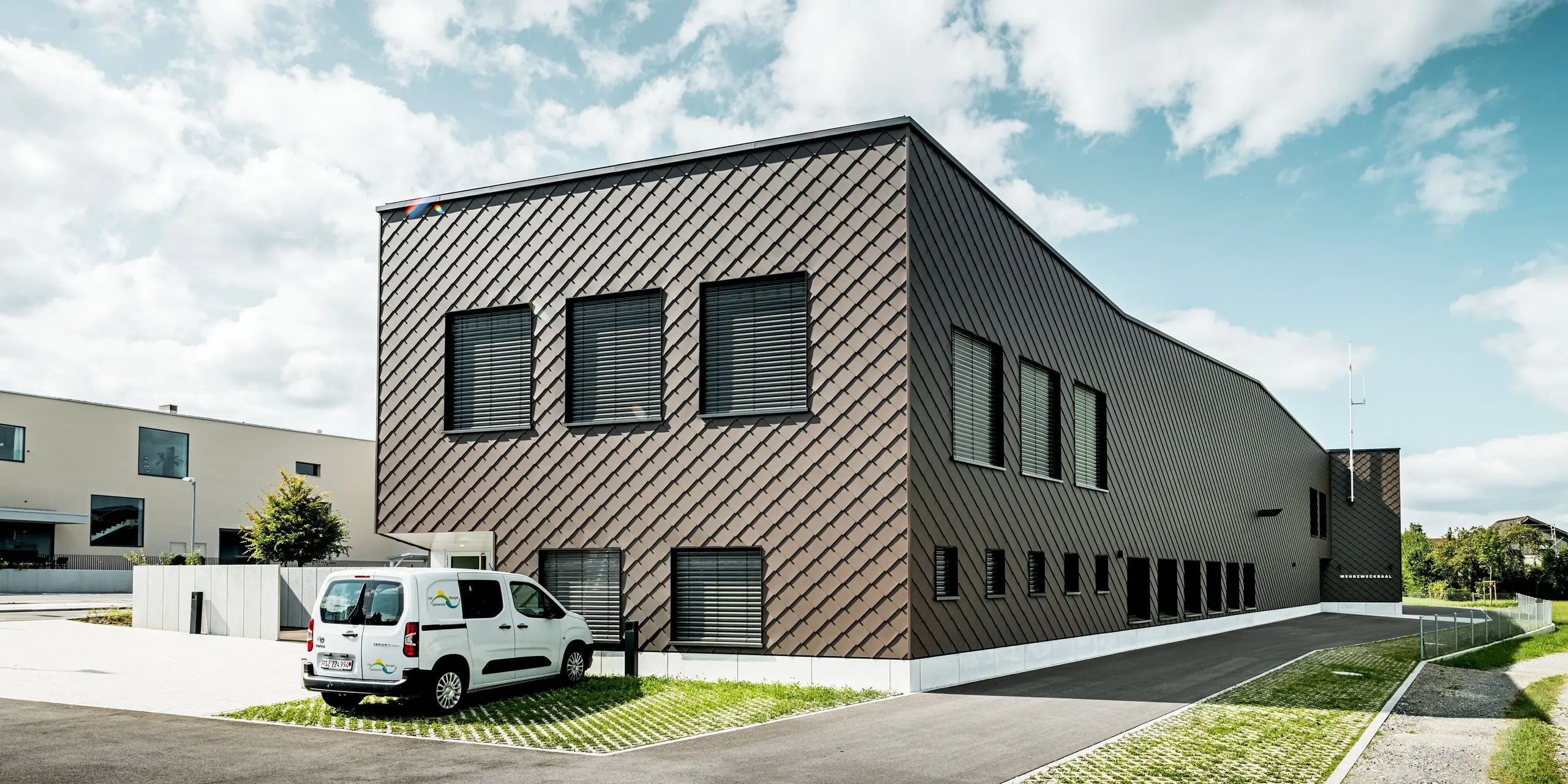 Architecture raffinée à Wangen, en Suisse : la vaste façade du bâtiment abritant la caserne de pompiers et la centrale électrique est entièrement revêtue de panneaux muraux PREFA de 29 x 29 cm, coloris P.10 Brun. Le motif losange uniforme enveloppe toute la structure, lui conférant une allure moderne et saisissante. La façade en aluminium durable impressionne par sa grande résistance aux intempéries, son faible besoin d’entretien et son aspect toujours impeccable.