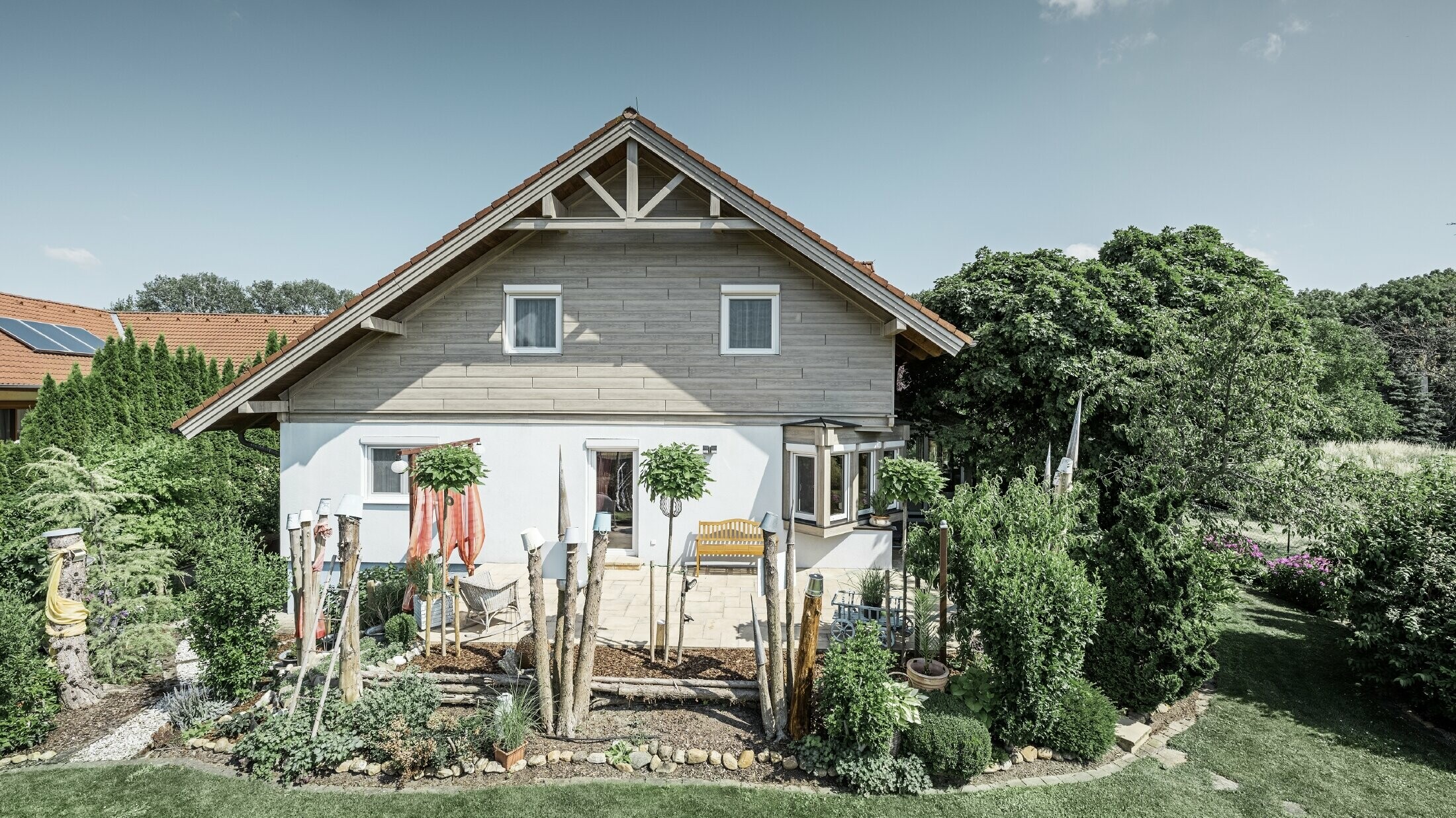 Maison individuelle rénovée avec un nouveau revêtement de pignon dans un style bois moderne gris-beige, combiné à une façade crépie, un toit en pente et un jardin bien entretenu.