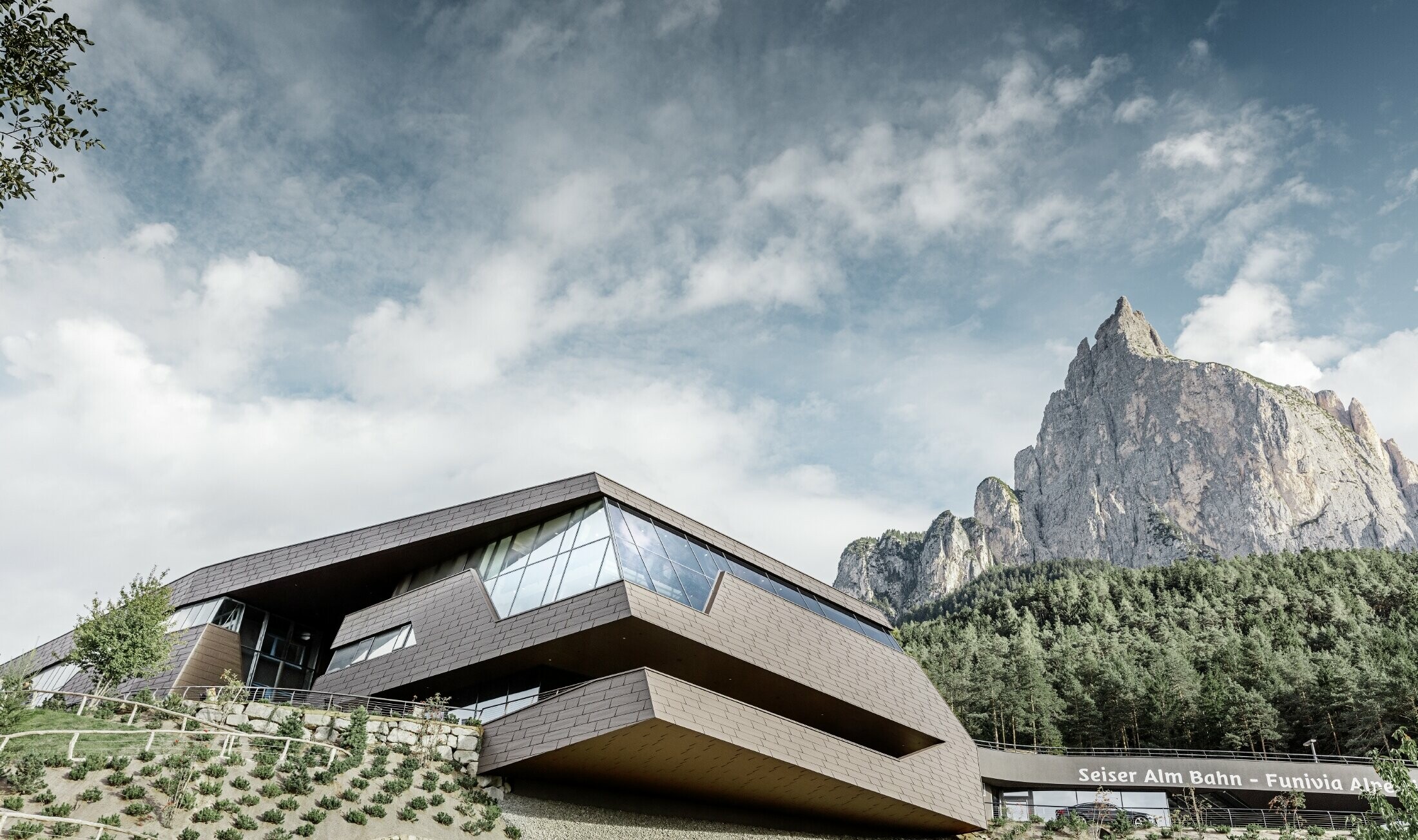 Gare de départ rénovée de la télécabine de l’Alpe di Siusi rappelant les Dolomites qui s’élèvent en toile de fond avec ses arêtes et ses surfaces irrégulières — Façade en aluminium PREFA (brun)