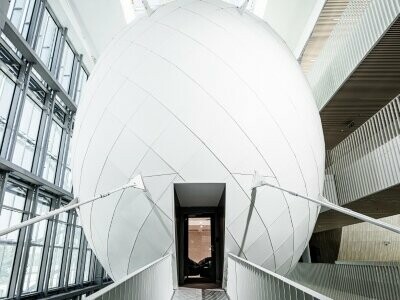 Un pont mène à l'entrée de l'œuf suspendu composé de bandes d'aluminium coloré en P.10 Blanc Prefa. L'œuf sera utilisé comme salle de séminaire.