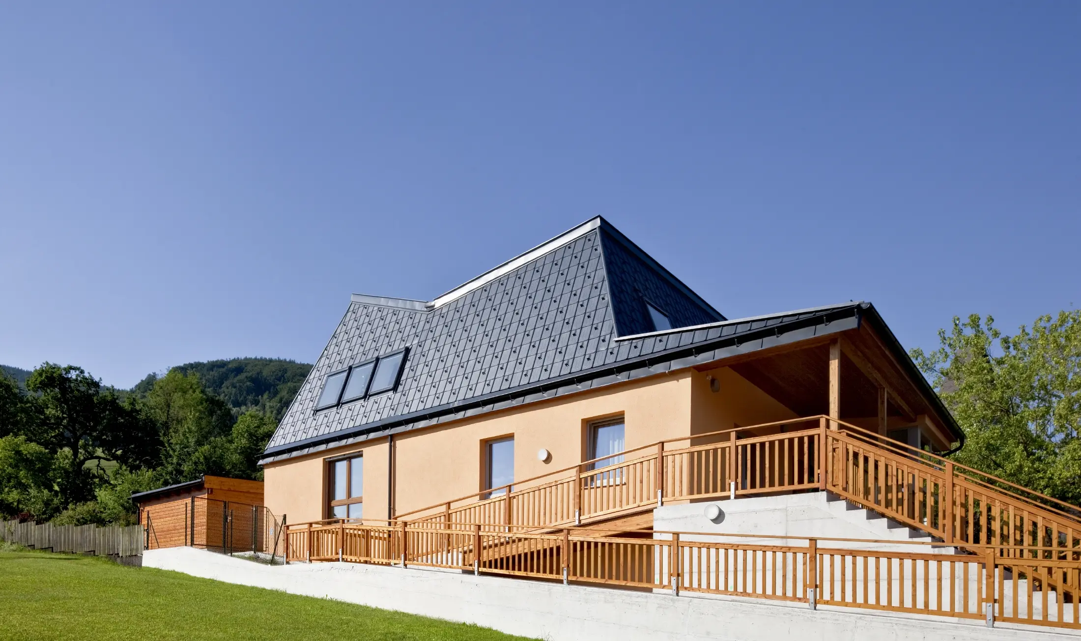 Maternelle avec façade en crépi orange et toiture à pans inclinés, recouverte de tuiles PREFA P.10 anthracite ;