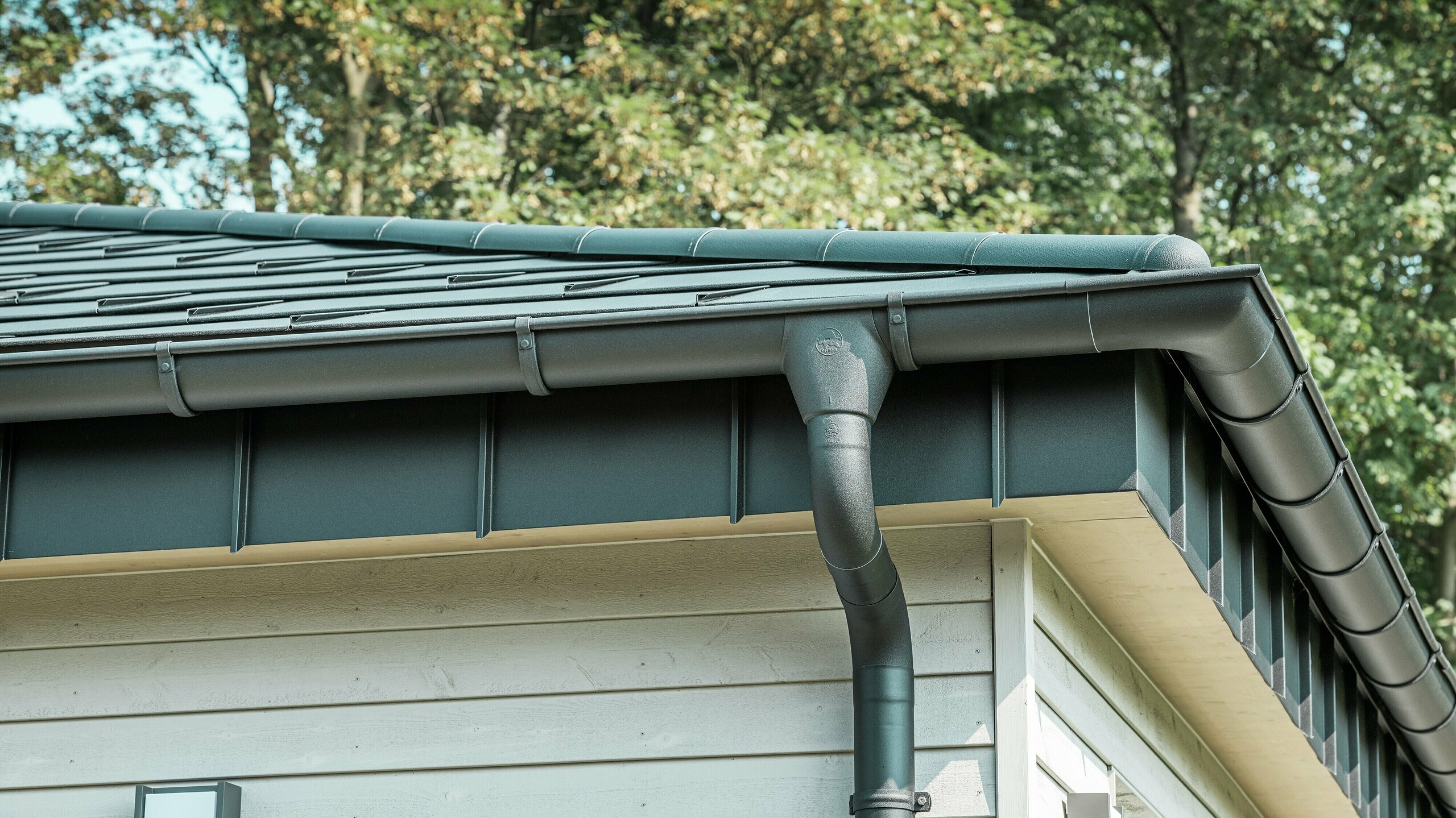 Gros plan du robuste système d'évacuation des eaux pluviales PREFA d'un bungalow à Rommerskirchen. La gouttière et le tuyau de descente de haute qualité P.10 noir offrent une protection optimale contre les intempéries. Durabilité et fonctionnalité se combinent avec un design élégant en aluminium.