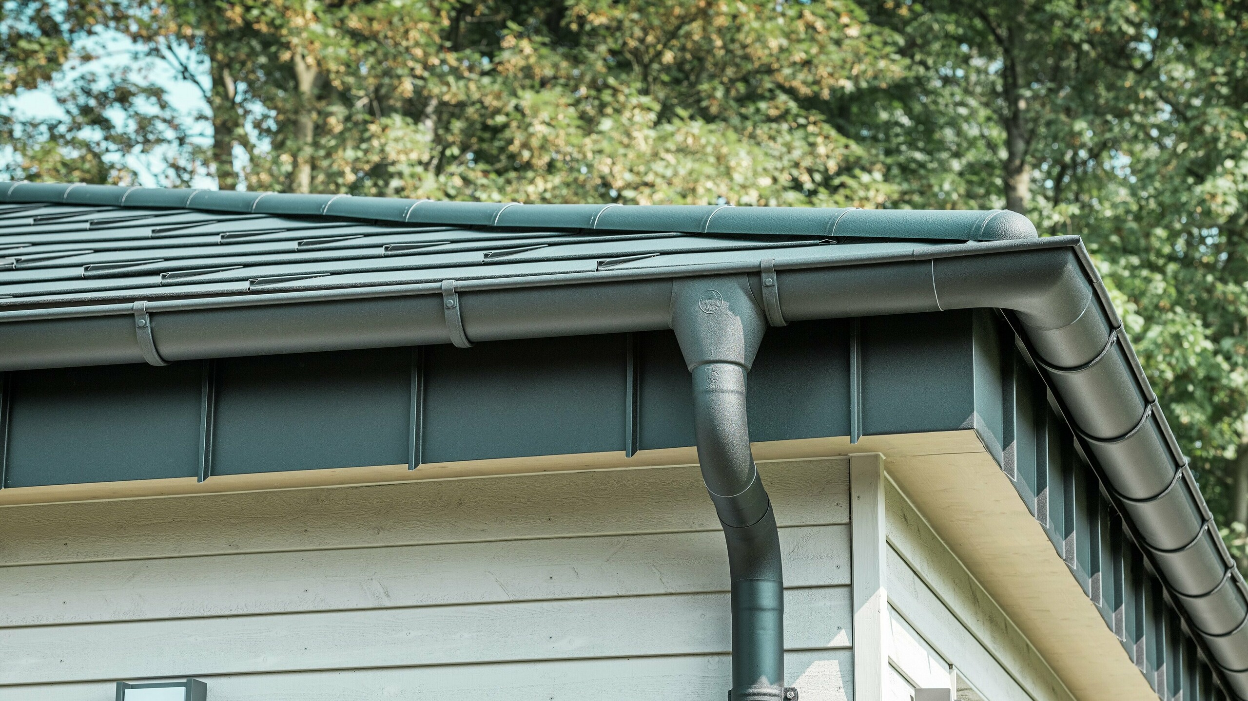 Gros plan du robuste système d'évacuation des eaux pluviales PREFA d'un bungalow à Rommerskirchen. La gouttière et le tuyau de descente de haute qualité P.10 noir offrent une protection optimale contre les intempéries. Durabilité et fonctionnalité se combinent avec un design élégant en aluminium.