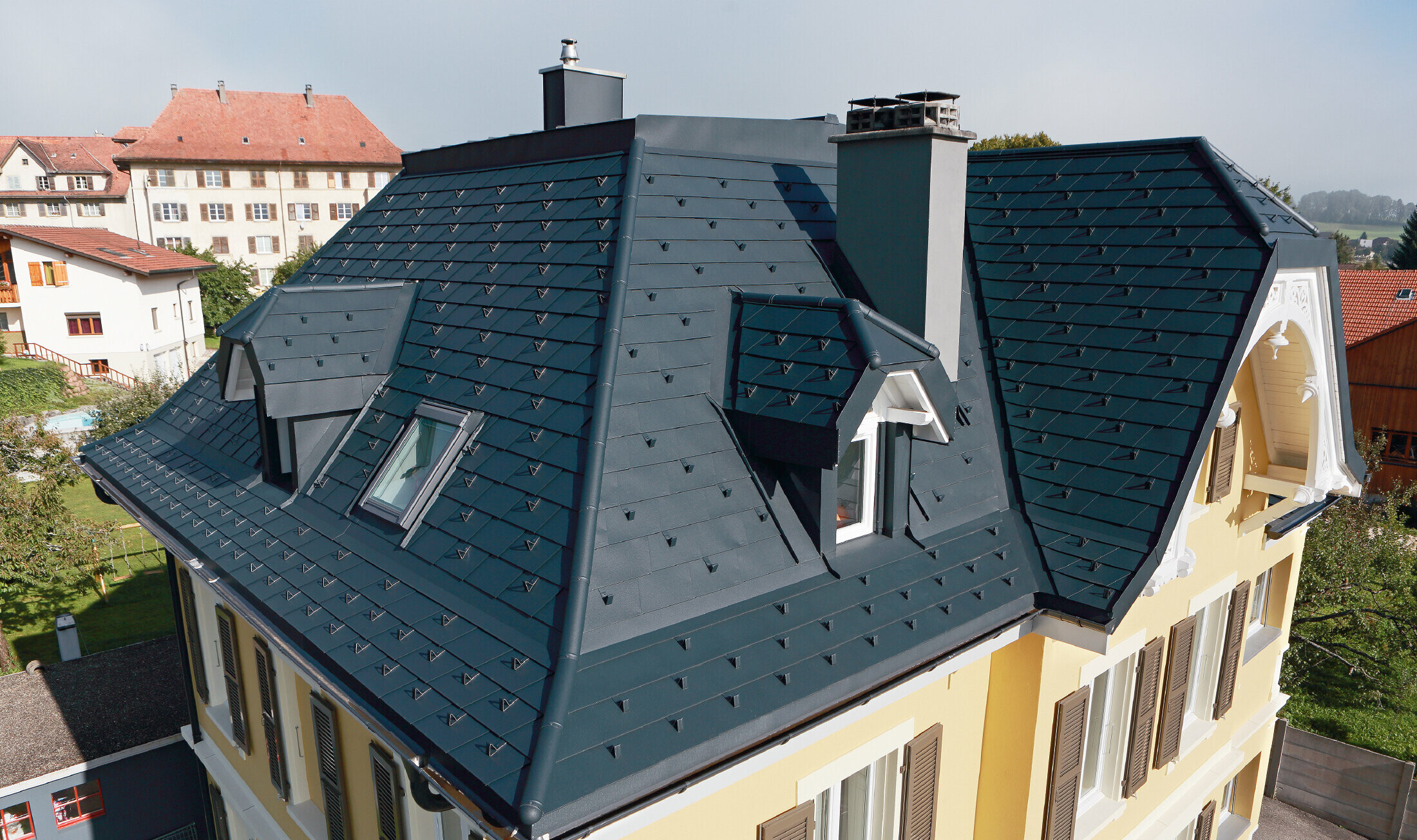 Villa en Suisse, le toit est doté de nombreuses noues et de petites lucarnes, le toit est recouvert de bardeaux en aluminium de PREFA dans la couleur P.10 anthracite