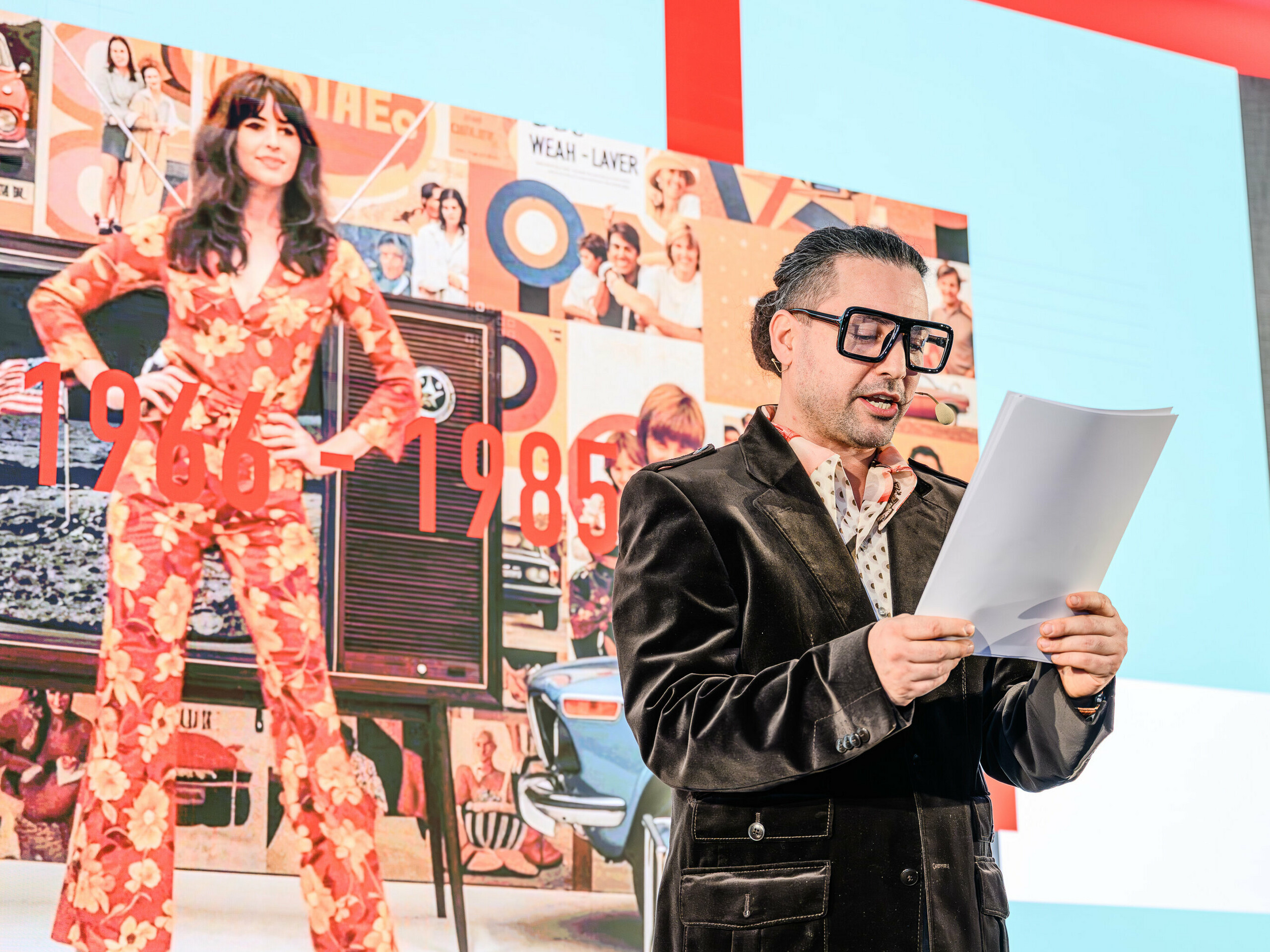 Un voyage dans le temps sur scène lors de la présentation PREFARENZEN 2026 : le charismatique Serkan Temel, dans un style rétro, guide le public à travers les décennies. L’accent est mis sur les années 1966 à 1985, représentées en arrière-plan par un collage d’icônes du design et de tendances sociales de cette époque. À l’image des produits PREFA, les tendances perdurent avec style et substance. La présentation démontre comment l’architecture d’hier inspire les solutions de demain – réinterprétées avec l’aluminium.