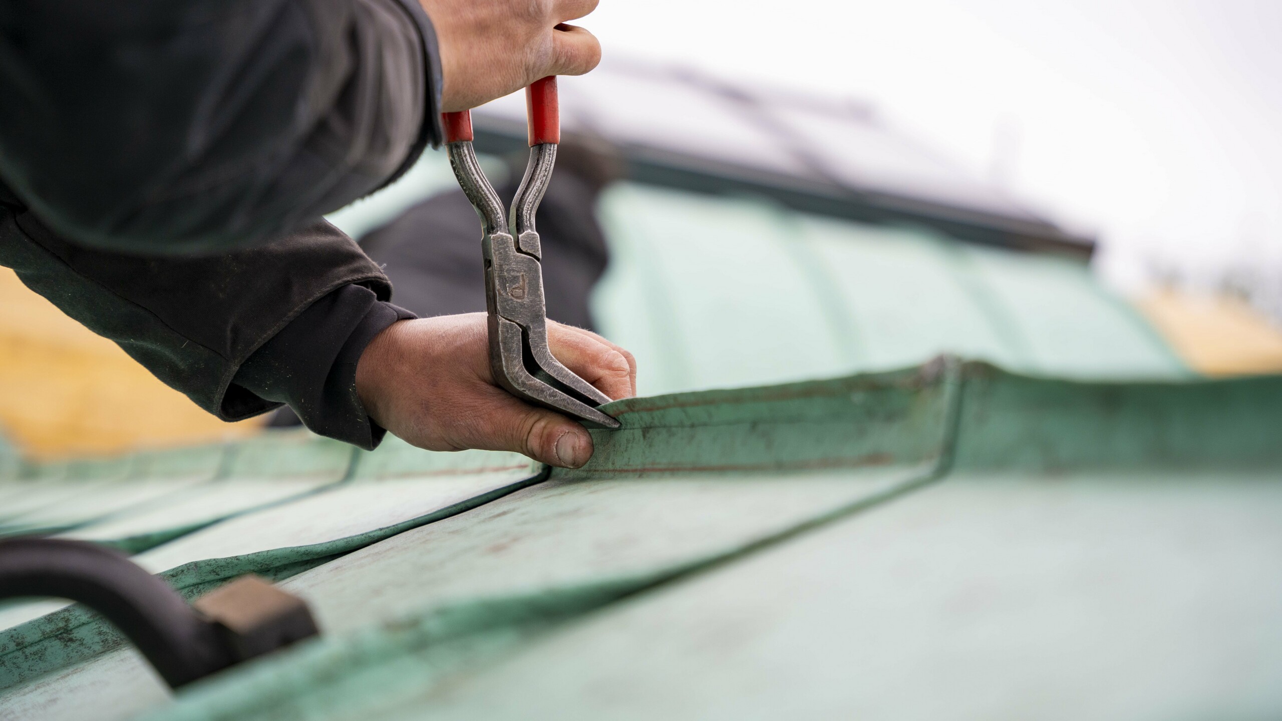 Zoom sur le geste technique de ce couvreur de l'entreprise Toiture Parisienne, en train de réaliser une agrafe avec le joint debout Prefalz dans la teinte P.10 vert-de-gris