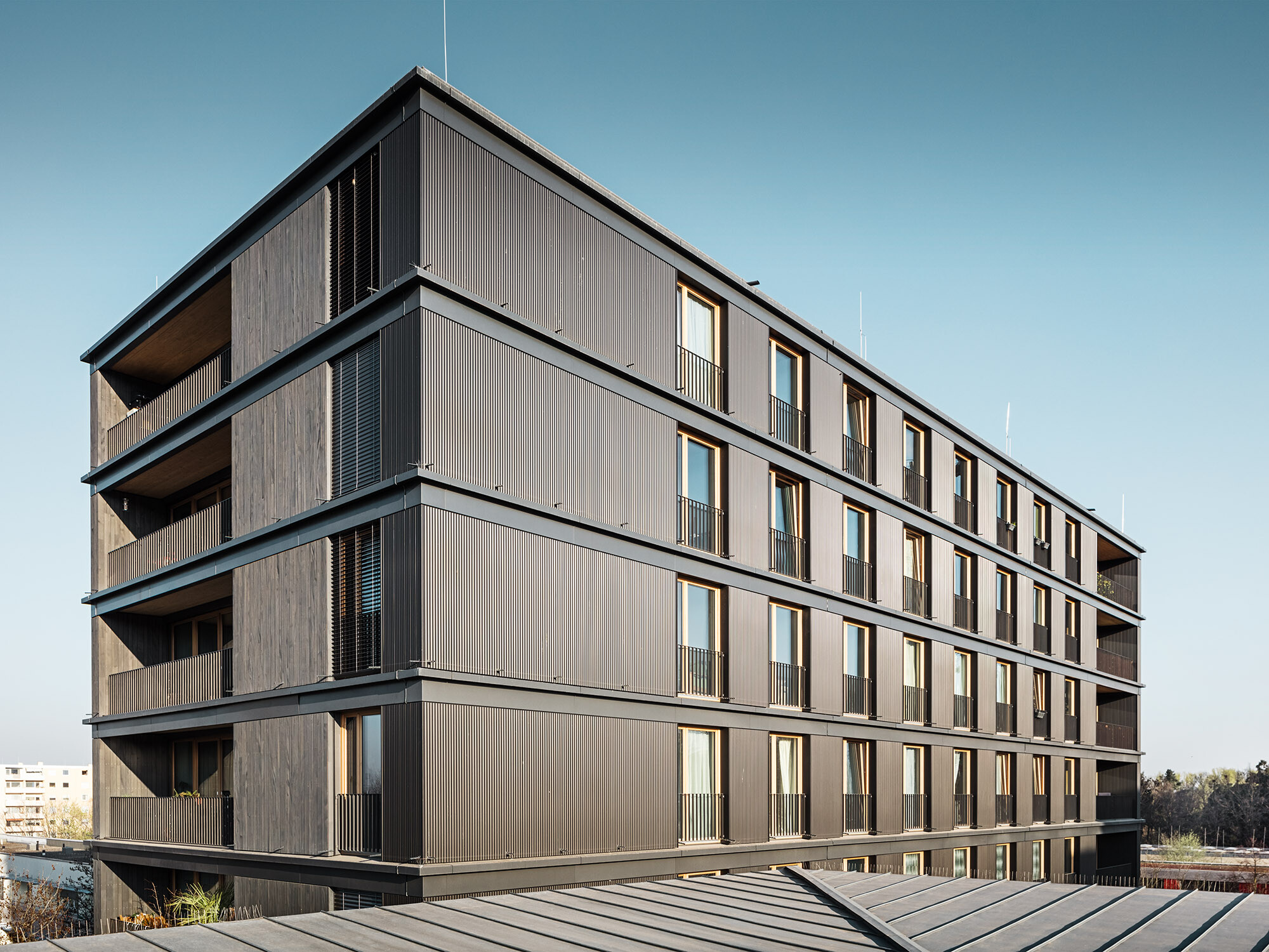 L'immeuble d'habitation et de bureaux vu de côté : le profil ondulé de PREFA et la façade en bois sont presque indiscernables.