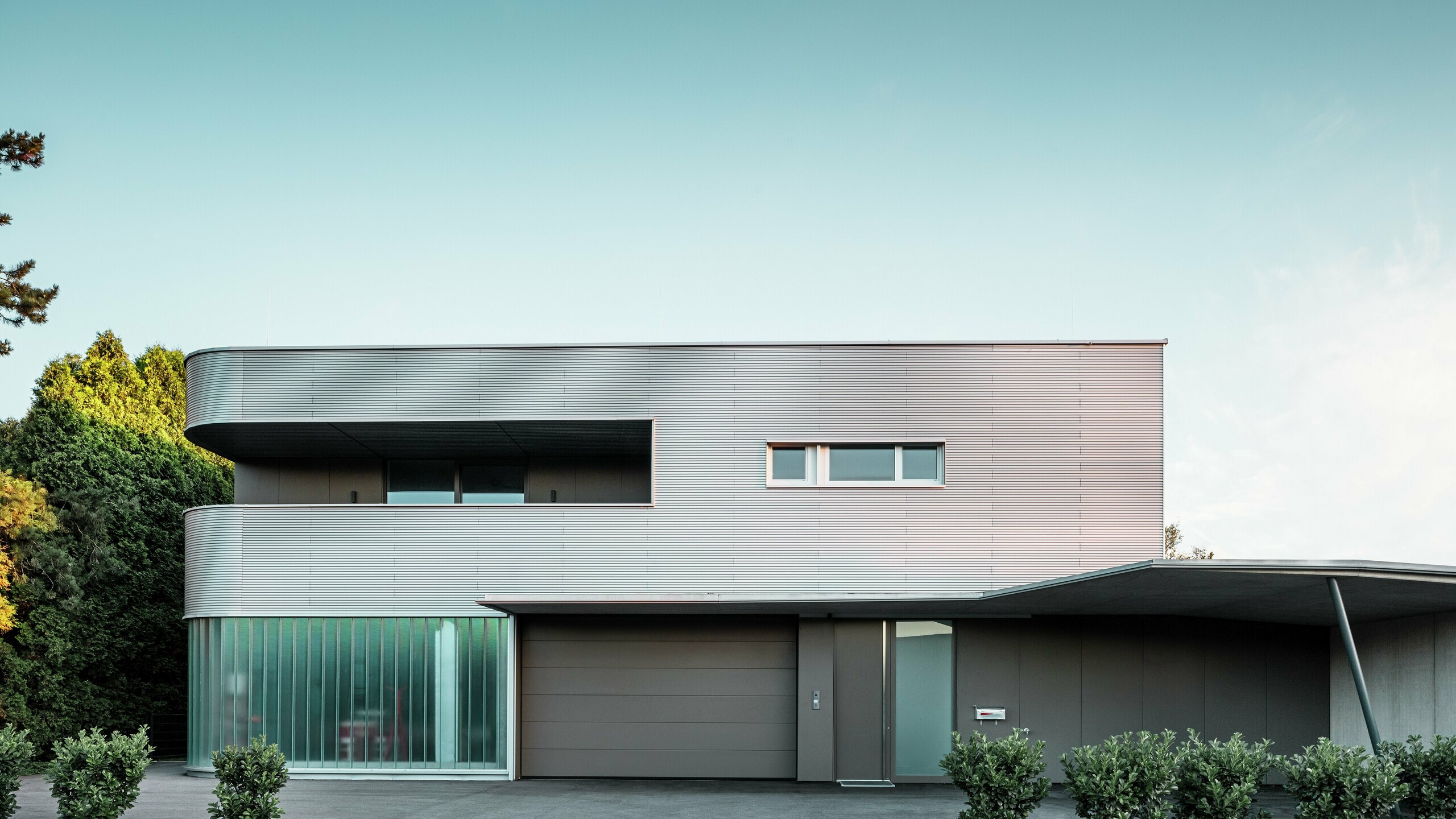 Maison moderne avec façade en aluminium naturel PREFA profil sinus et garage baigné de lumière naturelle.