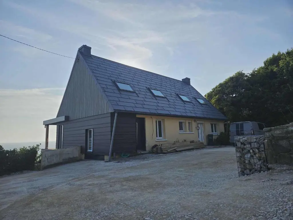 Vue d'ensemble de cette maison familiale située face à la mer, à Les Pieux. Elle a récemment été rénovée avec les produits de toiture PREFA : panneaux FX.12 et tuile solaire PREFA dans la teinte P.10 gris sombre.