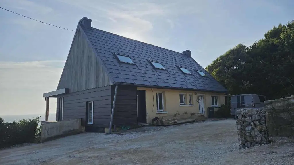 Vue d'ensemble de cette maison familiale située face à la mer, à Les Pieux. Elle a récemment été rénovée avec les produits de toiture PREFA : panneaux FX.12 et tuile solaire PREFA dans la teinte P.10 gris sombre.