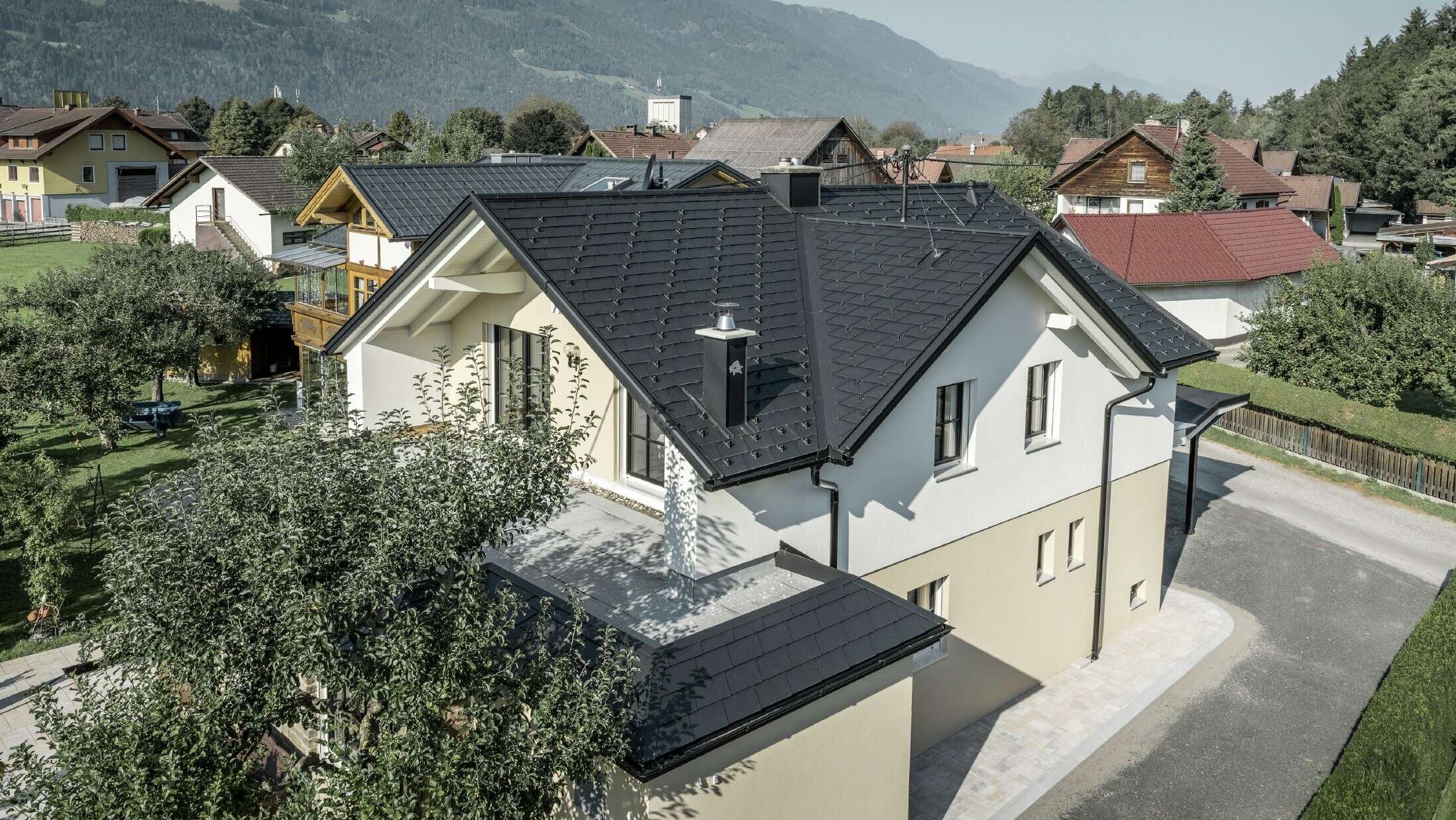 Maison individuelle traditionnelle avec toit en bâtière et grande lucarne, récemment rénovée. La toiture est recouverte de bardeaux noirs PREFA.