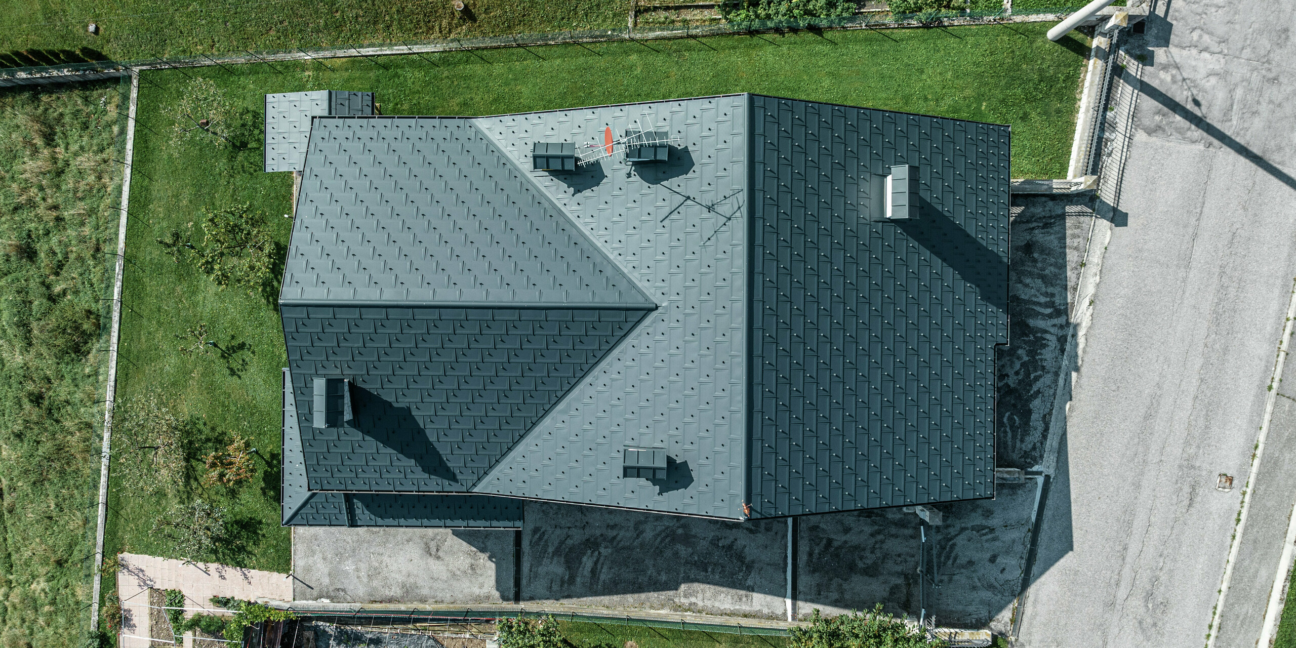 Prise de vue par drone d'une maison familiale à Gallio avec une couverture de toit PREFA de haute qualité composée de panneaux de toiture R.16 en P.10 gris sombre. La solution de toiture en aluminium impressionne par son aspect moderne, sa résistance extrême aux intempéries et sa durabilité. Les crochets pare-neige offrent une sécurité supplémentaire dans les régions alpines. La finition précise et le système de drainage sophistiqué garantissent une protection optimale contre la pluie et la neige. Un toit nécessitant peu d’entretien pour des générations.