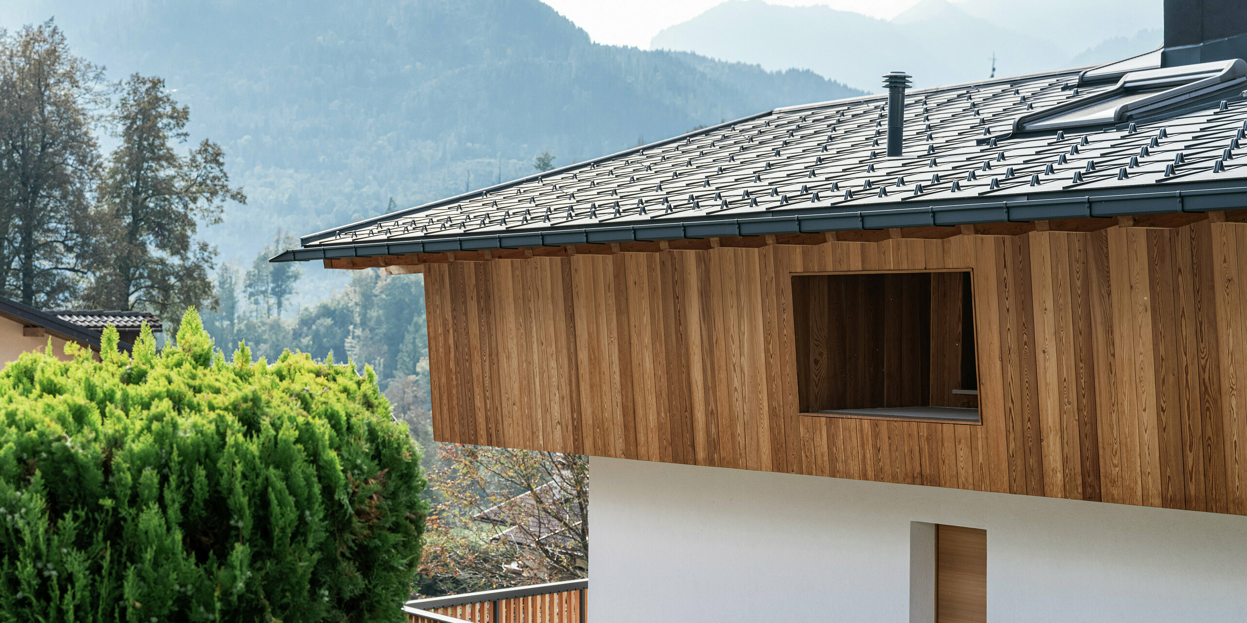 Vue détaillée d'une maison familiale traditionnelle à Agordo, en Italie, avec une façade en bois naturel et des R.16 PREFA robustes en P.10 anthracite. Le toit en aluminium durable avec pare-neige offre une protection optimale contre les intempéries. La combinaison d'une façade en bois naturel à l'étage supérieur et d'une façade en plâtre blanc au rez-de-chaussée donne à la maison un aspect chaleureux et moderne. Les lignes épurées et les matériaux de haute qualité s'intègrent harmonieusement dans l'environnement alpin.