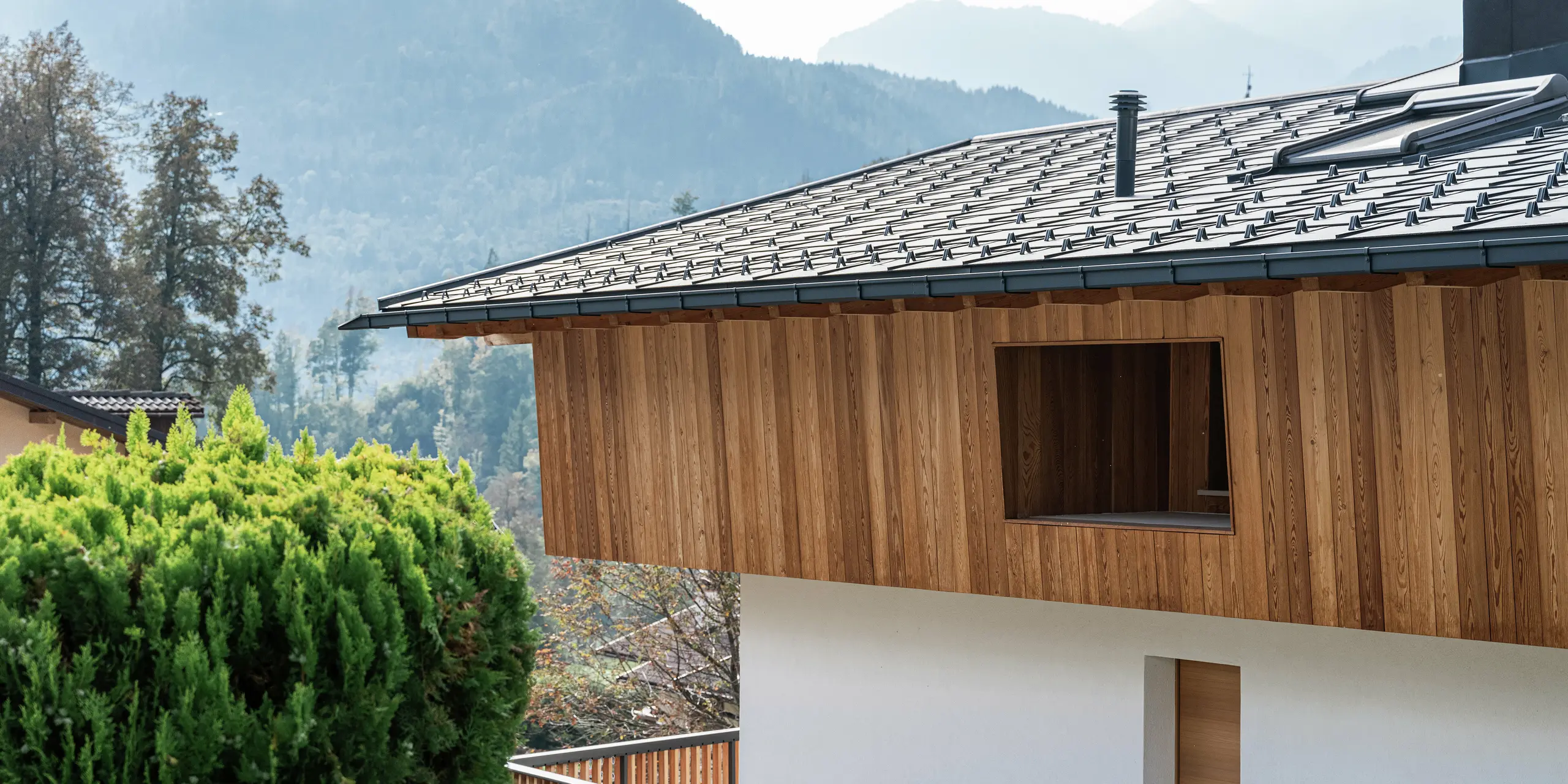 Vue détaillée d'une maison familiale traditionnelle à Agordo, en Italie, avec une façade en bois naturel et des R.16 PREFA robustes en P.10 anthracite. Le toit en aluminium durable avec pare-neige offre une protection optimale contre les intempéries. La combinaison d'une façade en bois naturel à l'étage supérieur et d'une façade en plâtre blanc au rez-de-chaussée donne à la maison un aspect chaleureux et moderne. Les lignes épurées et les matériaux de haute qualité s'intègrent harmonieusement dans l'environnement alpin.