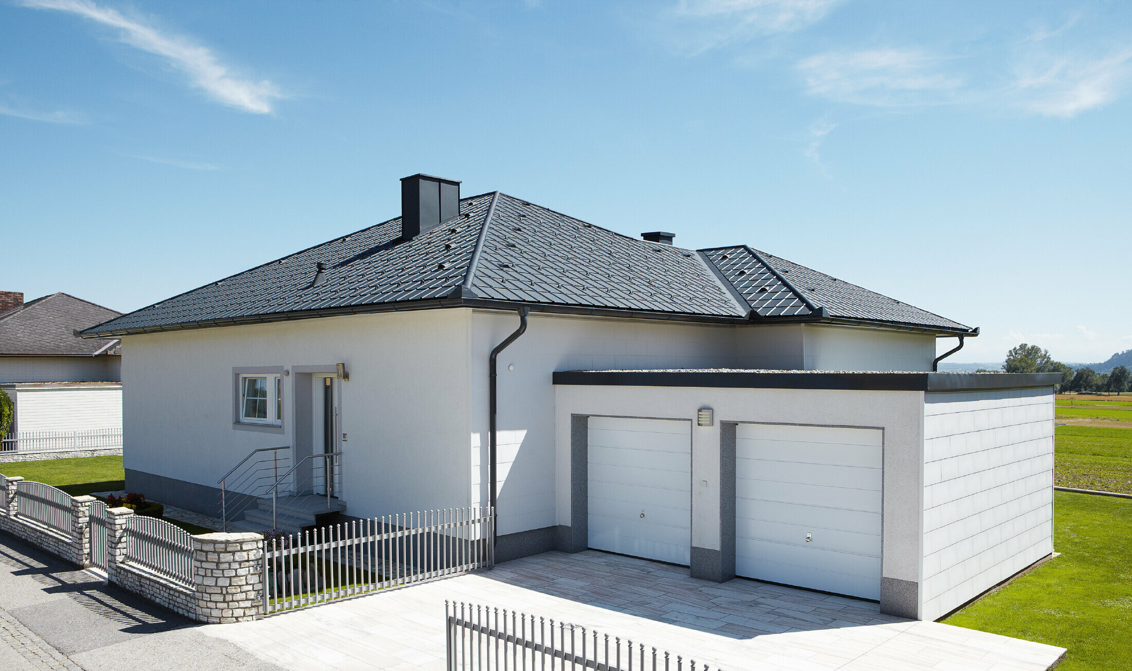 Le bungalow nouvellement construit avec un toit en toile a été recouvert de tuiles PREFA en P.10 anthracite. Un garage double a été construit à droite, la photo a été prise depuis la rue.