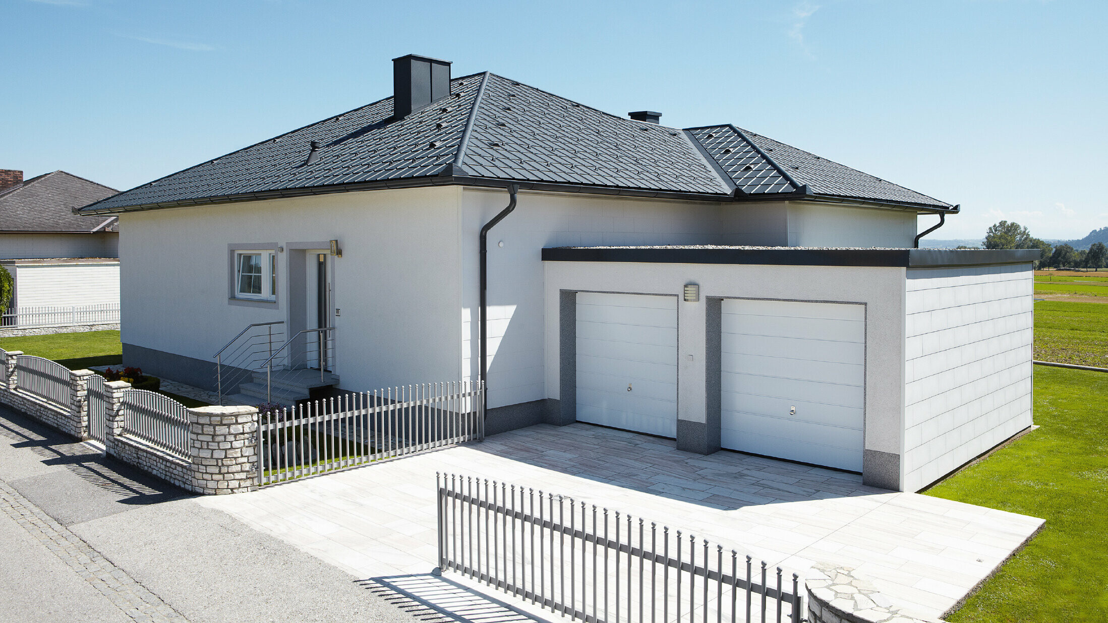 Le bungalow nouvellement construit avec un toit en toile a été recouvert de tuiles PREFA en P.10 anthracite. Un garage double a été construit à droite, la photo a été prise depuis la rue.