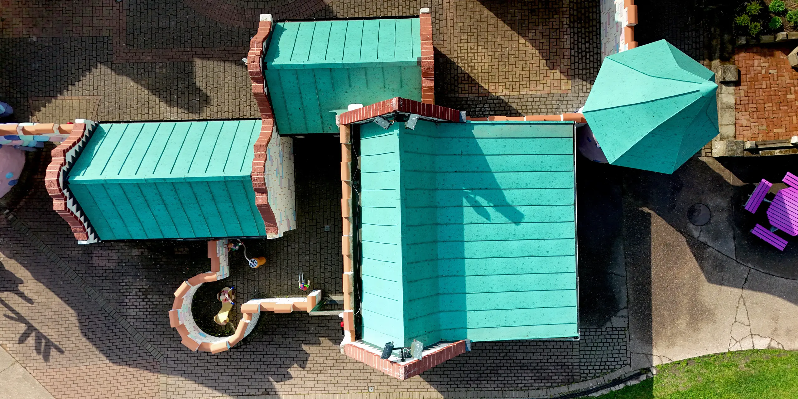 Une vue aérienne dynamique de l'architecture ludique du château de Sundown Adventureland, mettant en valeur les multiples toitures aux pentes variées, aux arêtes vives et aux joints debout parfaitement structurés. Les toitures en aluminium PREFALZ, couleur P.10 vert de gris, confèrent aux bâtiments une allure élégante et précise, et soulignent avec brio la géométrie complexe. Grâce à leur grande malléabilité, même les détails les plus exigeants peuvent être réalisés avec précision, tandis que le système PREFA impressionne par sa durabilité, sa résistance à la corrosion et sa protection fiable contre les intempéries.