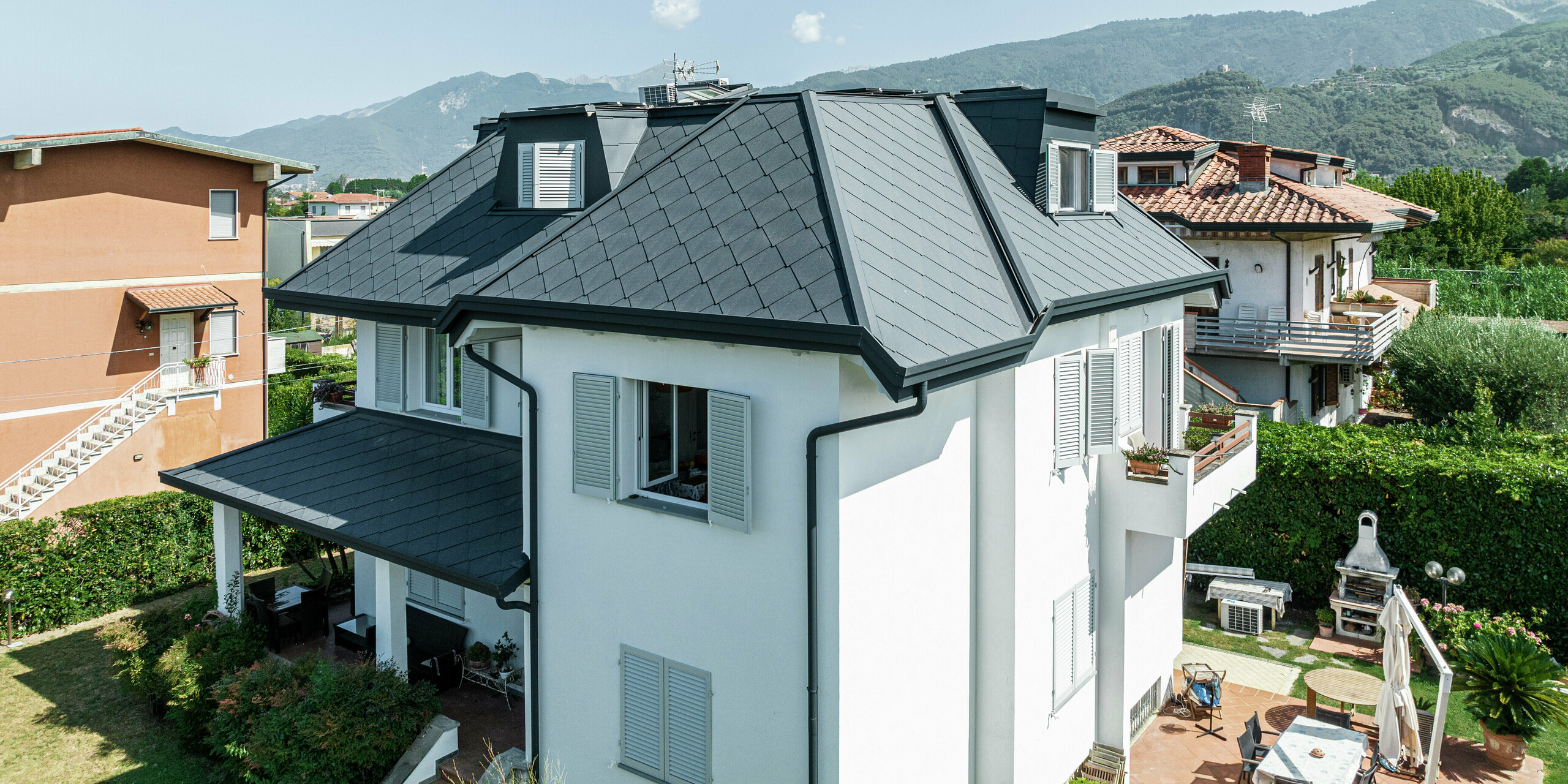 Gros plan de l'élégant toit d'une maison familiale en Italie, recouvert de losanges de toiture 44 × 44 en P.10 gris pierre. Les lignes claires et la toiture en aluminium de haute qualité soulignent le design moderne de la maison familiale de Montignoso. Grâce aux matériaux PREFA robustes, le toit est non seulement visuellement attrayant, mais également extrêmement résistant aux tempêtes, à la corrosion et aux rayons UV. La toiture sombre forme un contraste élégant avec la façade claire et s'intègre harmonieusement dans l'environnement.