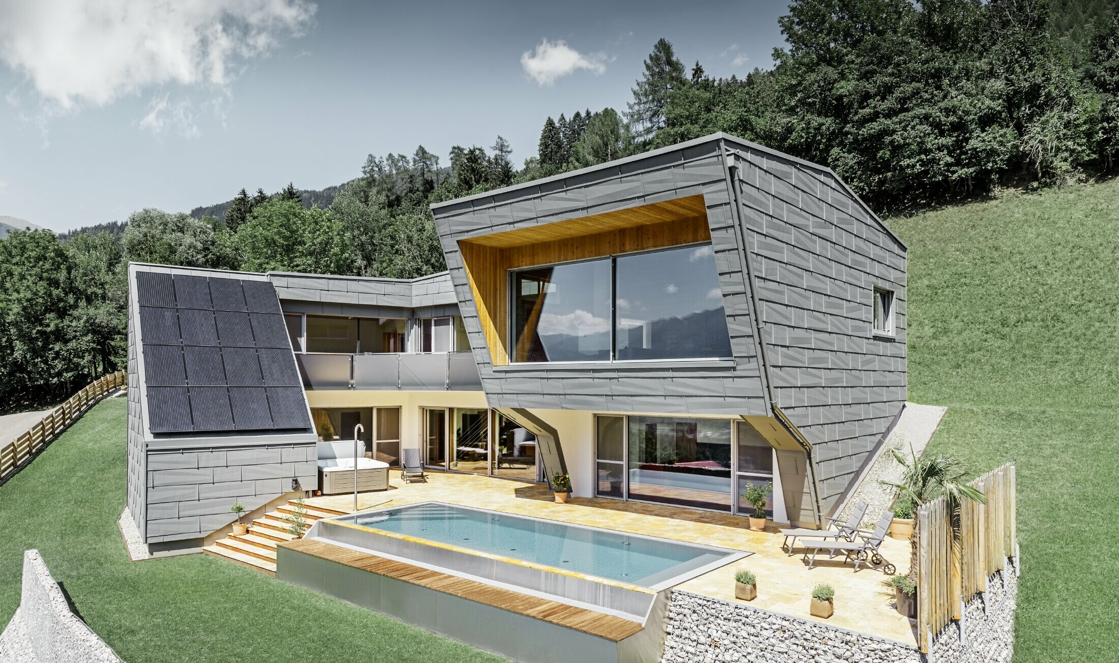 La maison individuelle moderne à flanc de coteau avec piscine a été recouverte de panneaux de façade FX.12 de PREFA couleur P.10 gris souris.