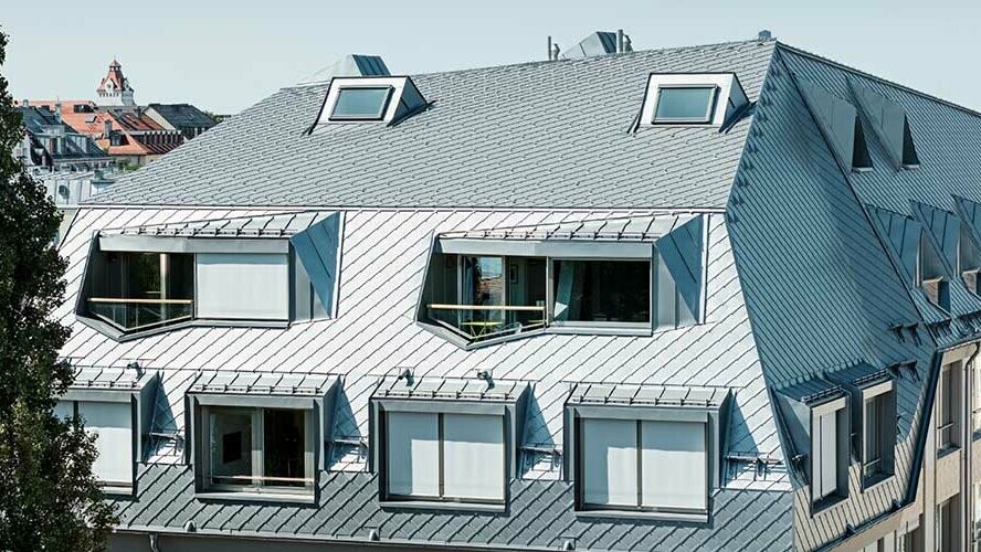 Combles d’un bâtiment résidentiel et commercial à Munich, recouvert de losanges de toiture PREFA 29 × 29 de couleur gris aluminium normalisé