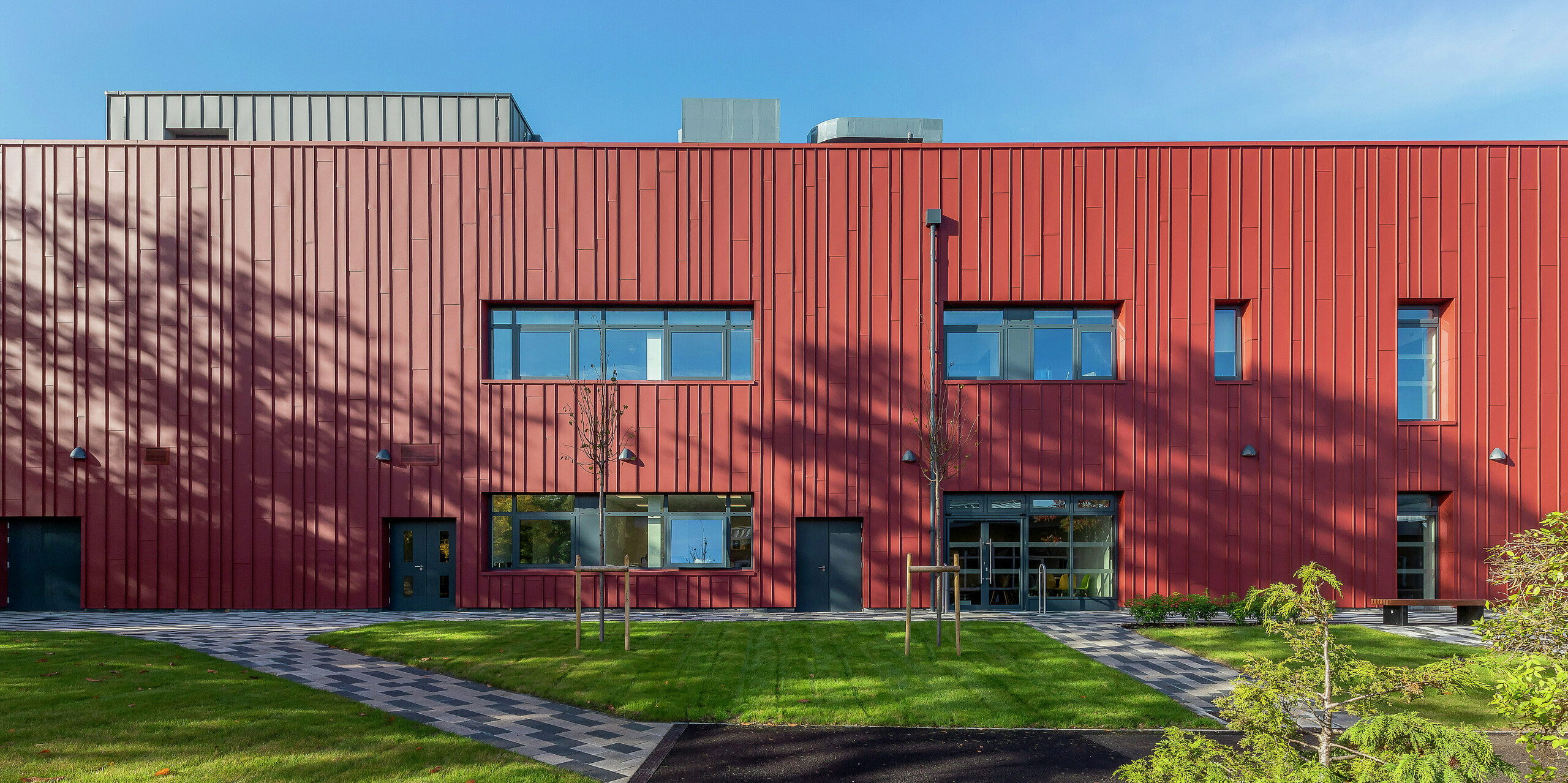 Conception de façade moderne avec PREFALZ : Le Soldiers' Centre de Pirbright impressionne par son revêtement à joint debout de haute qualité en PREFALZ en P.10 rouge oxyde. La combinaison élégante avec les revêtements de fenêtre en anthracite P.10 confère au centre social de l'armée une apparence saisissante. Ici, fonctionnalité et design se rencontrent – ​​un concept architectural durable avec de l’aluminium durable.