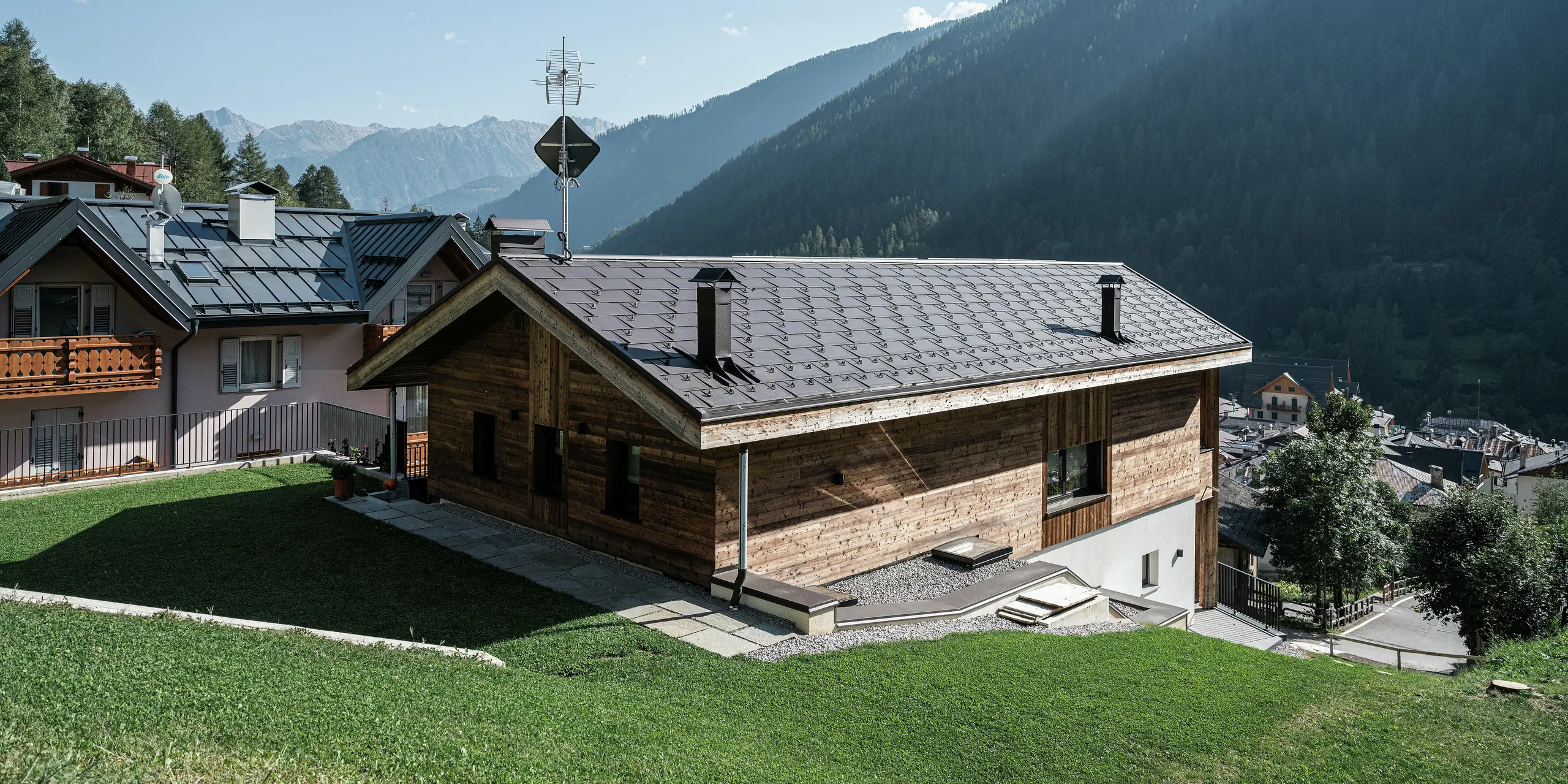 Arrière d'une maison de montagne moderne à Cogolo, dans le Val di Sol italien, avec des R.16 PREFA durables en P.10 brun. Le toit robuste en aluminium s'intègre parfaitement dans le paysage alpin et protège de manière fiable le bâtiment de la neige, du vent et des intempéries. Des lignes claires et une capacité de charge maximale font de ce toit la solution idéale pour les régions de haute altitude.
