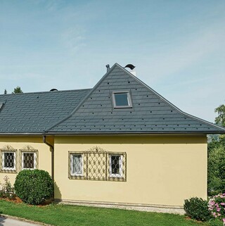 Maison individuelle avec toit en croupe et façade en plâtre jaune; Le toit á été recouvert de bardeau anthracite PREFA.